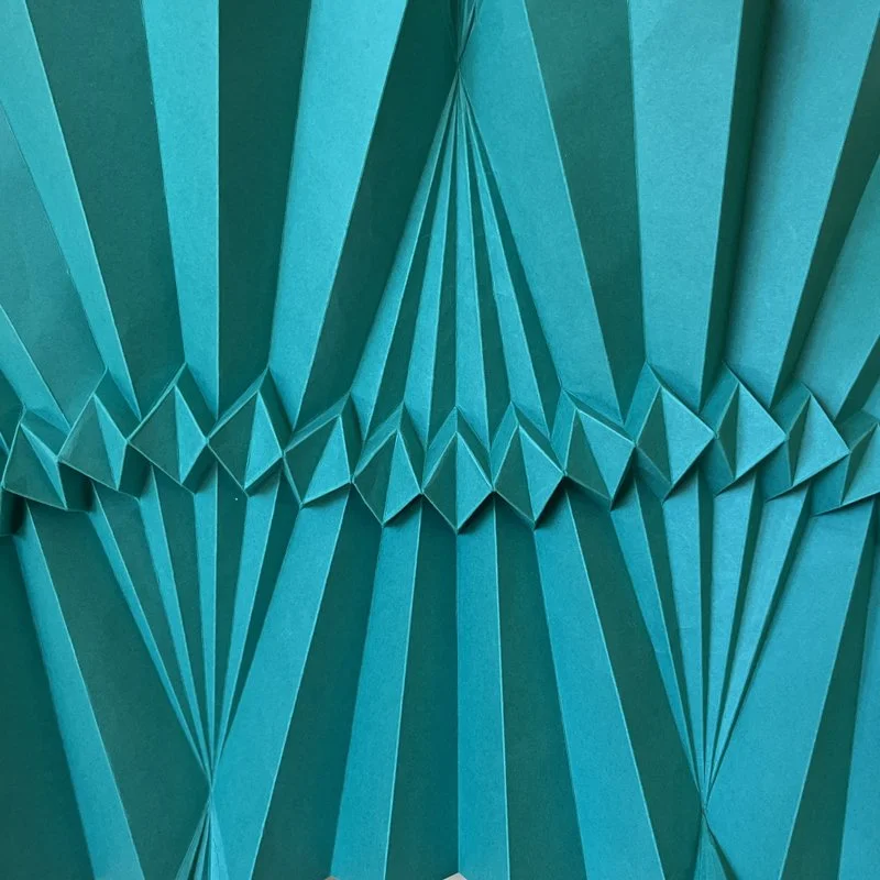 Close-up of a turquoise paper sculpture with folded geometric patterns.