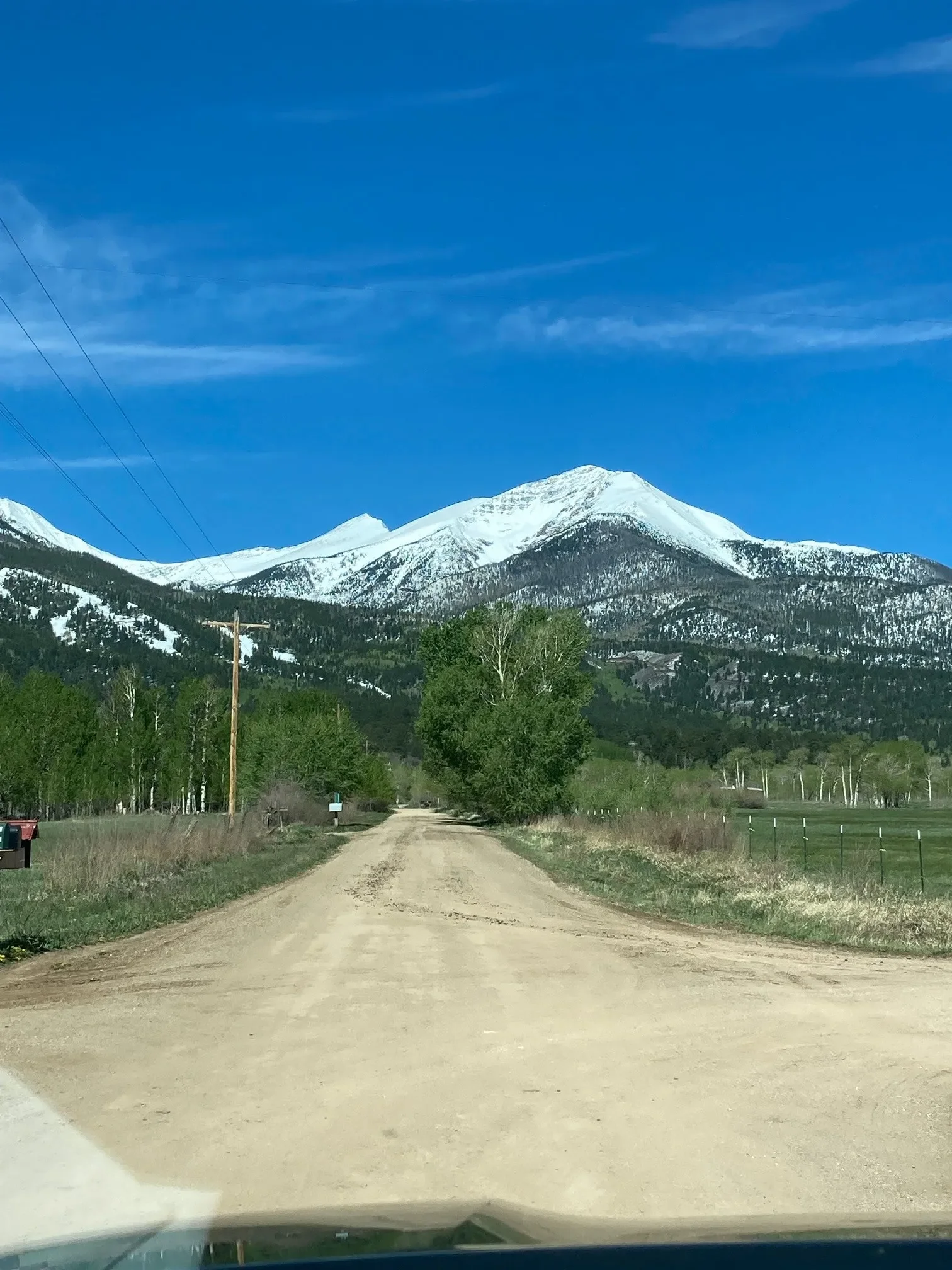 View of snow-capped mountains in the distance with a dirt road in the foreground and a clear blue sky.