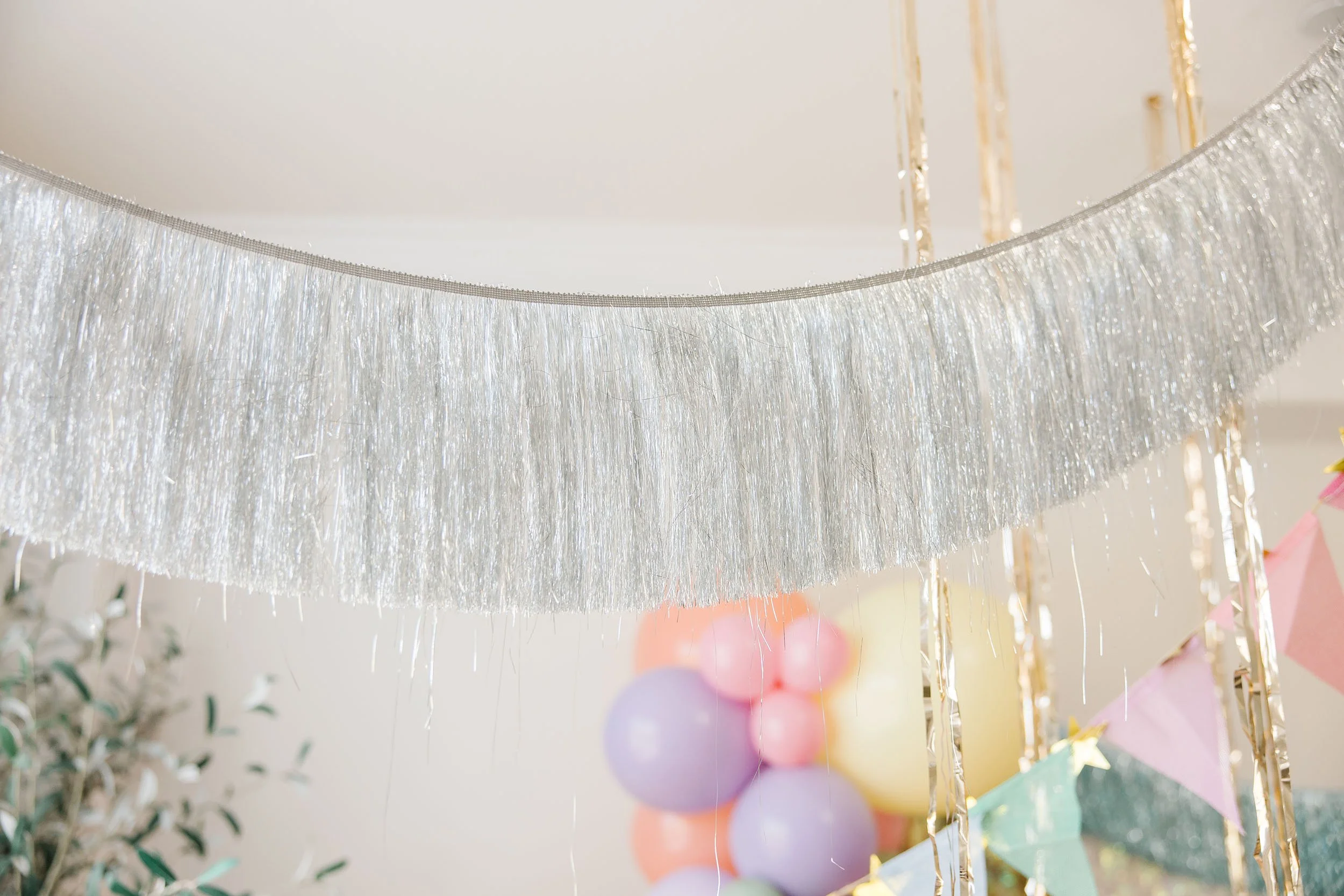 Silver fringe party decoration hanging above colorful pastel balloons