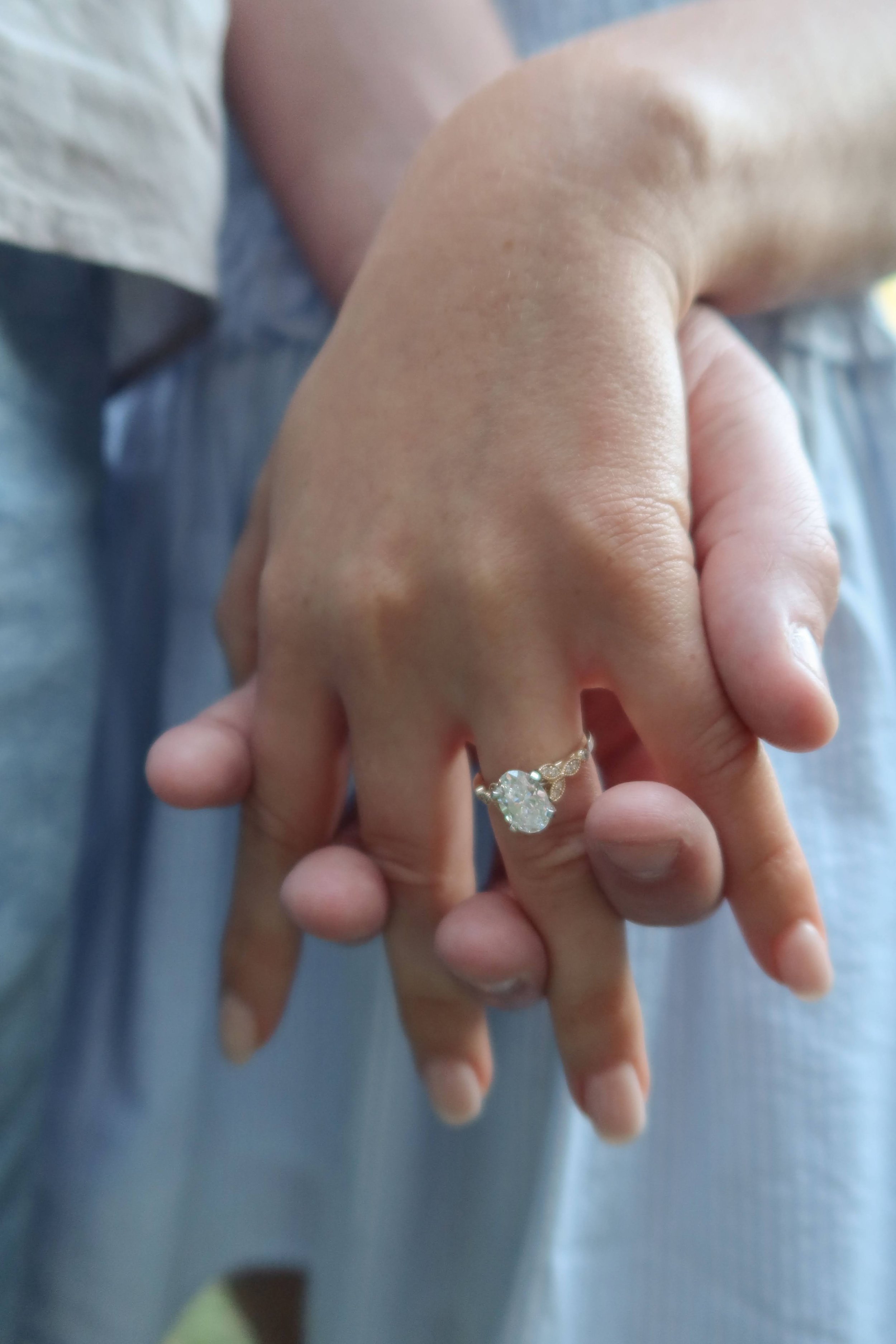 Close-up of two hands intertwined, one of which displays an engagement ring with a large diamond.