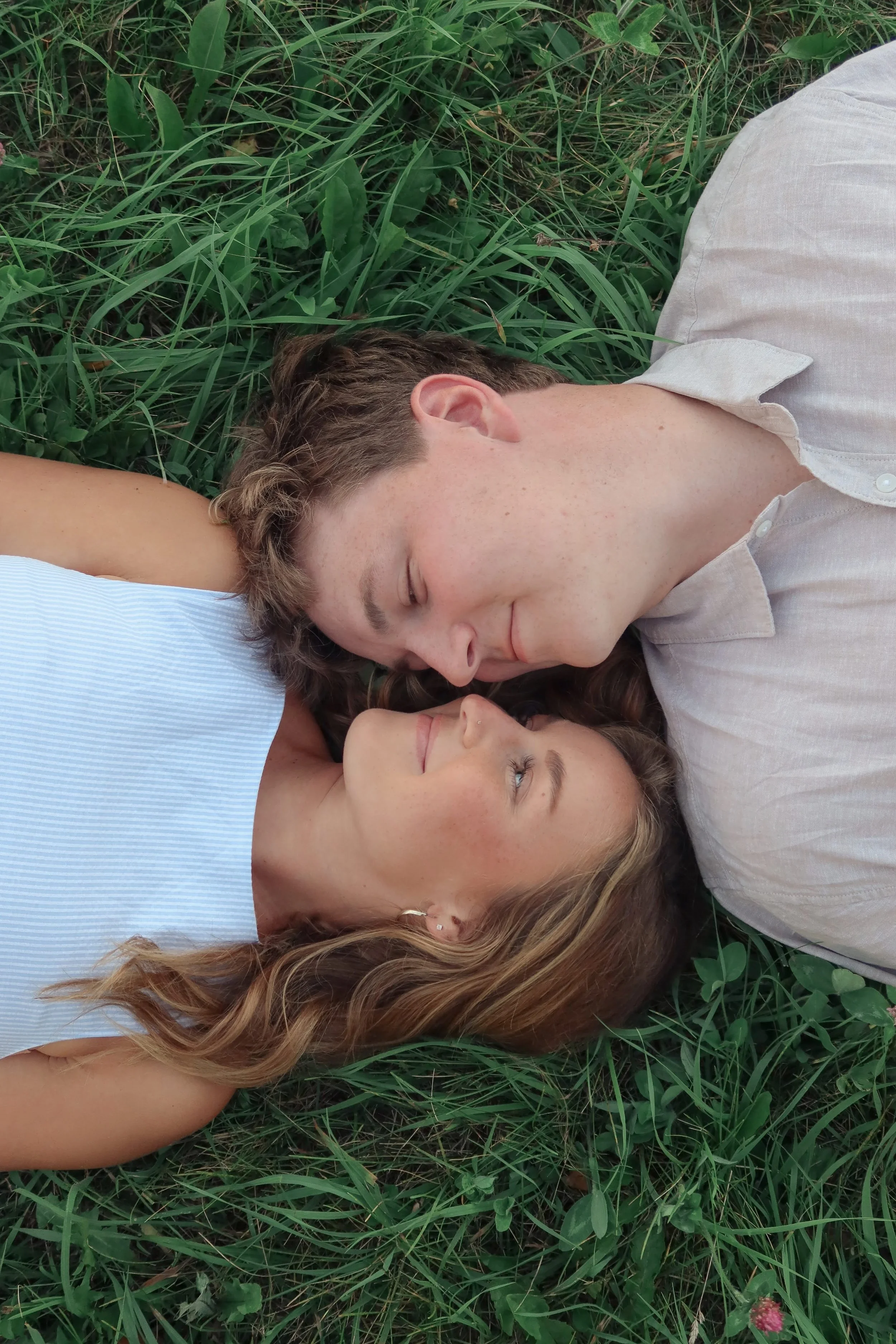 A man and a woman lying down on grass with their heads close together, eyes closed, in a relaxed and peaceful pose.