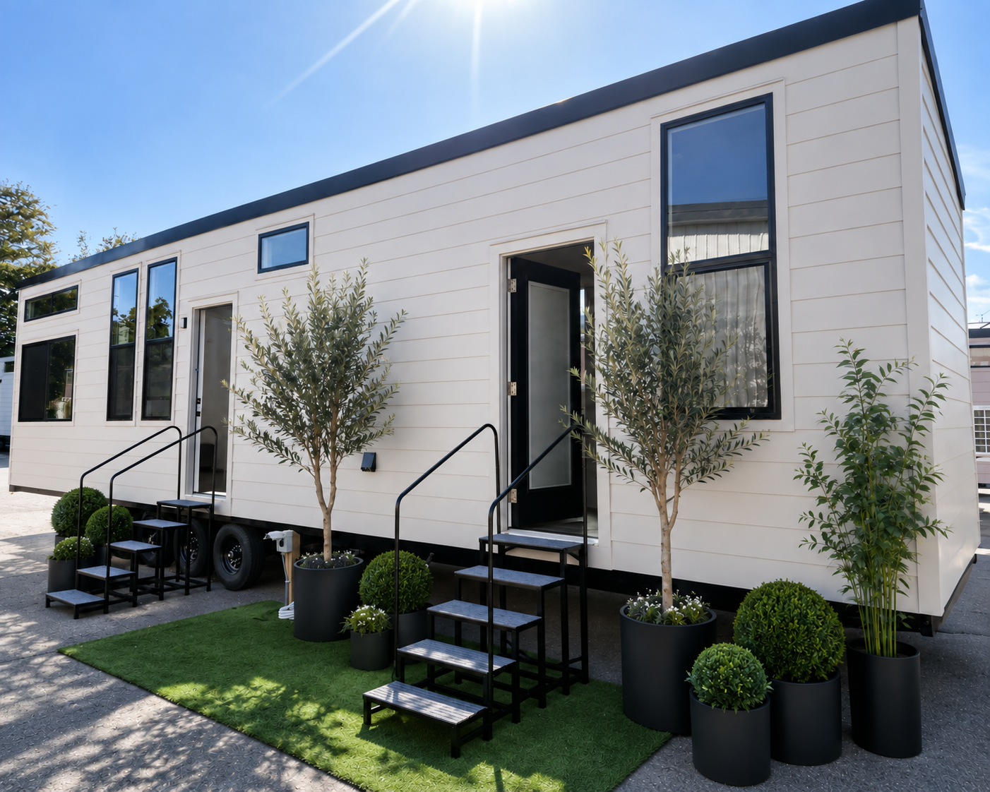 Forever 40-foot 2B tiny home on wheels with white siding, tall black-trimmed windows, and two entrances with metal steps.