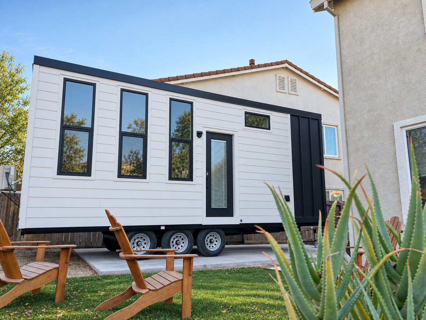 Forever 24-foot Studio tiny home on wheels with white fiber cement siding, a black accent wall, and tall windows.