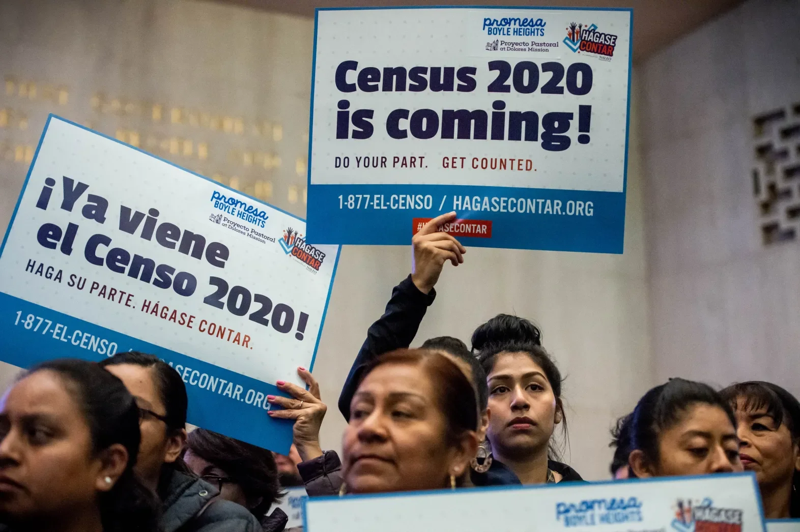 People holding signs at a community event, with signs in both English and Spanish promoting the 2020 Census and encouraging participation.