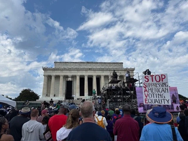 Crowd gathering at the Lincoln Memorial during a protest or rally, with a large sign reading 'Stop Suppressing American Voting Equality' in front.