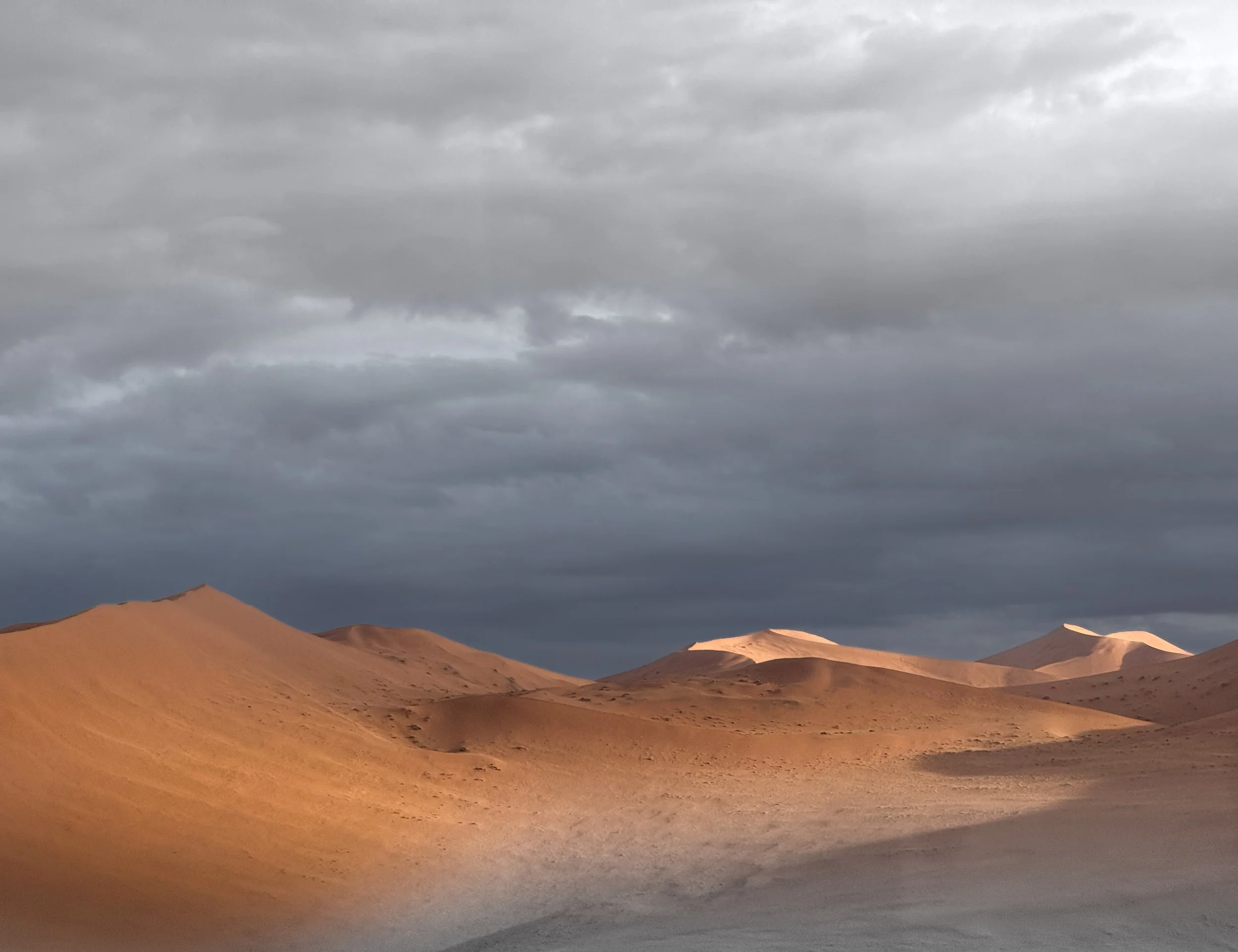 Desert landscape with sand dunes under a cloudy sky.