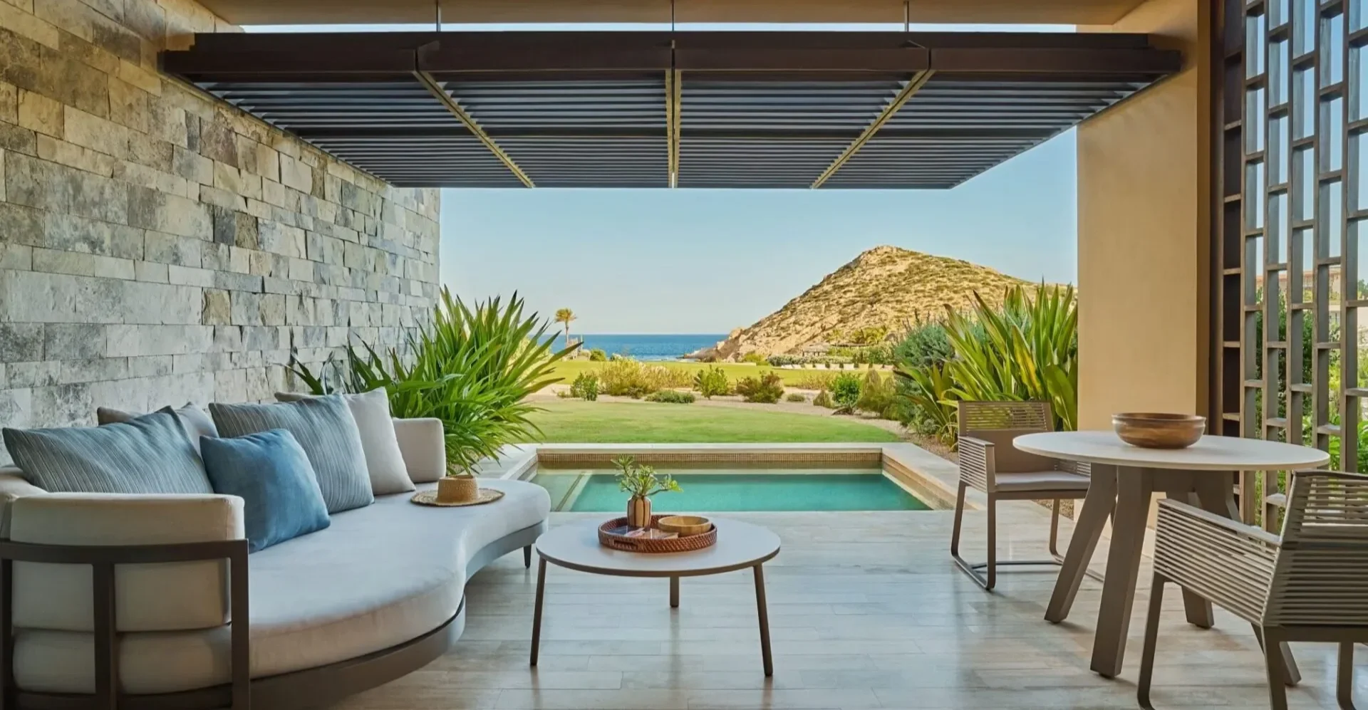 Modern outdoor patio with seating, a small pool, lush plants, and a scenic mountain view in the distance.