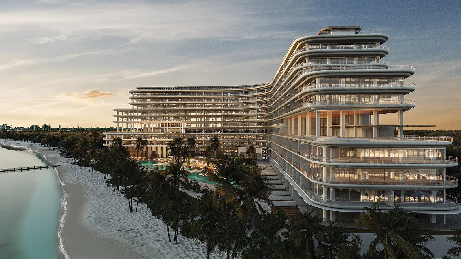 Modern beachfront hotel with multiple glass balconies, surrounded by palm trees, overlooking a sandy beach and ocean, at sunset.