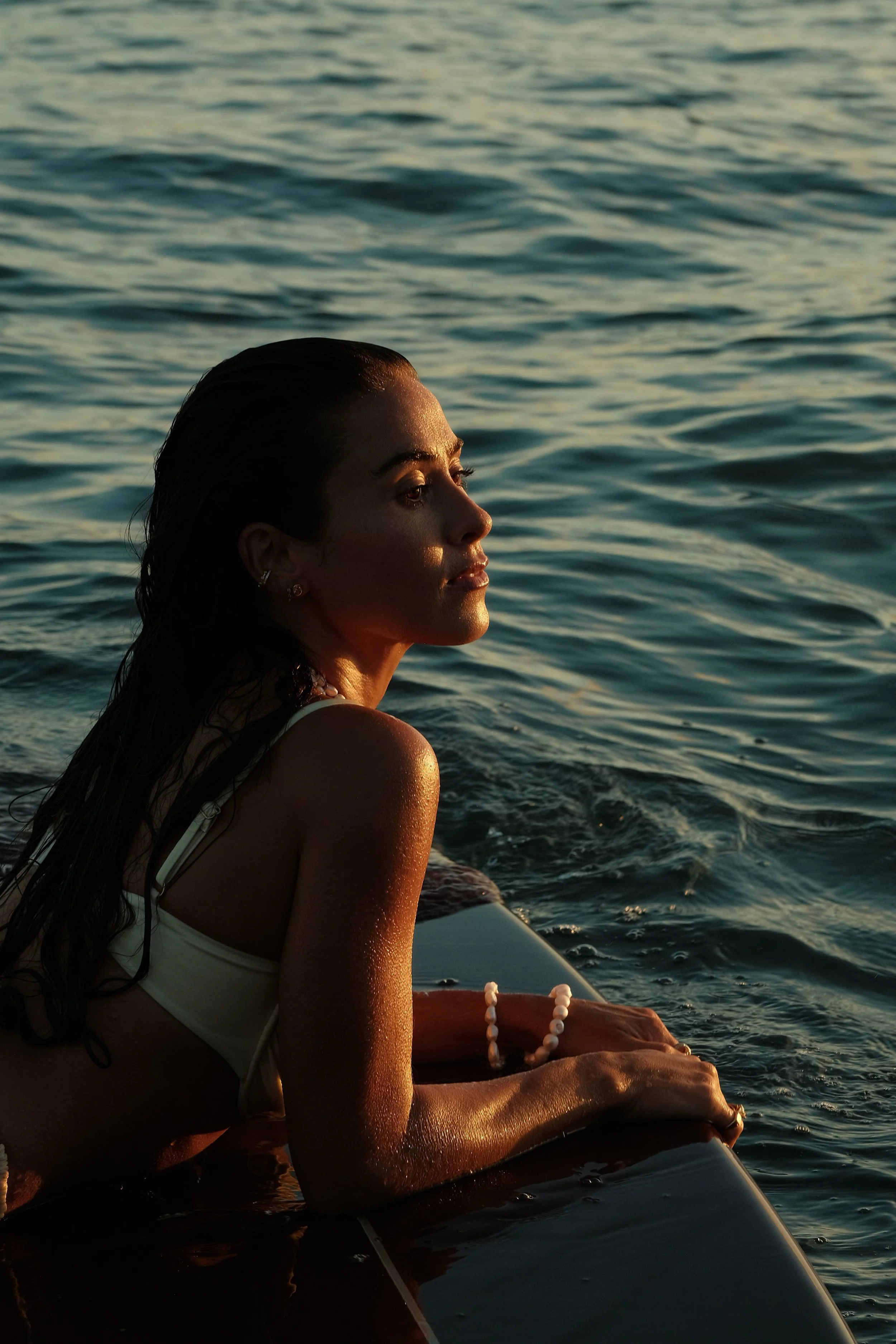 A woman with wet hair and earrings sitting on a boat at sunset, looking out over the water.