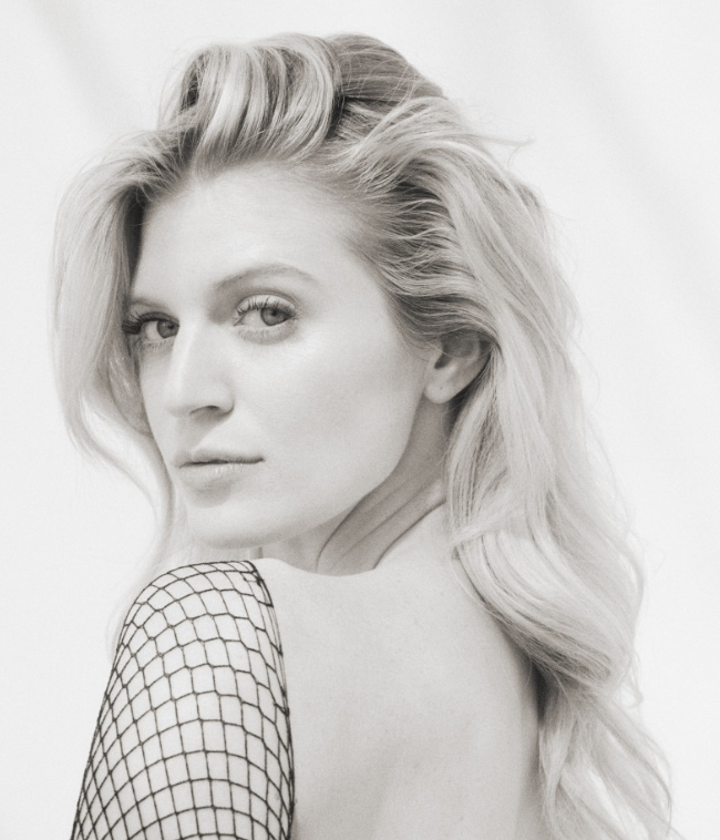Black and white portrait of a woman with wavy blonde hair, looking over her shoulder.