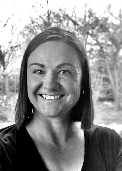 Black and white portrait of a smiling woman outdoors.