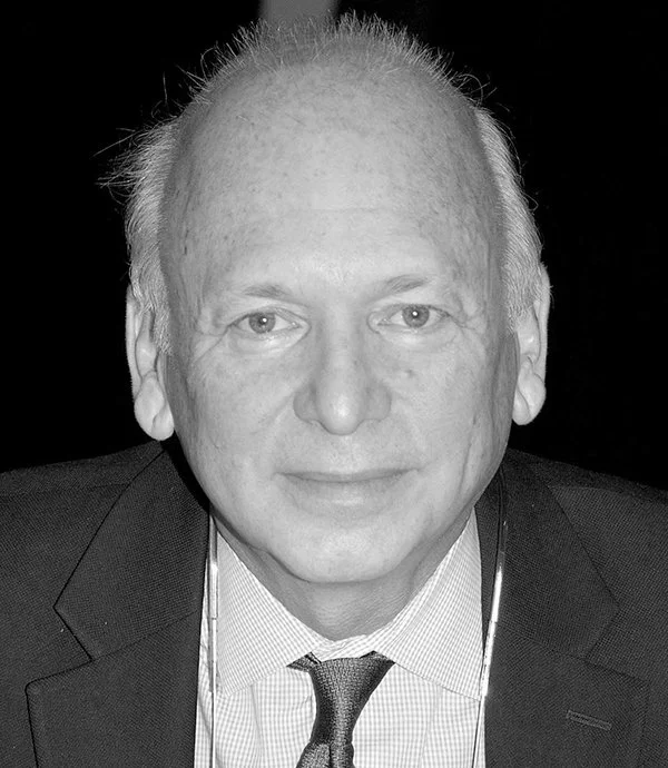 Black and white portrait of a bald man in a suit and tie, looking at the camera.