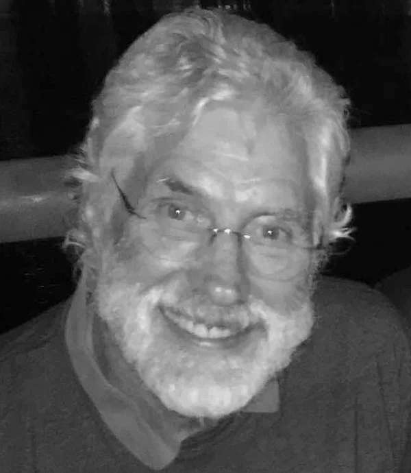 Elderly man with glasses and a white beard smiling.