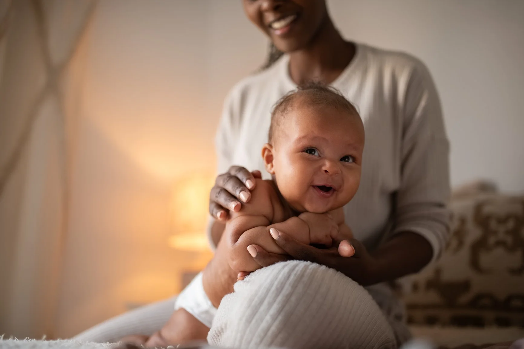 A smiling woman holding a happy baby with a cozy indoor background.