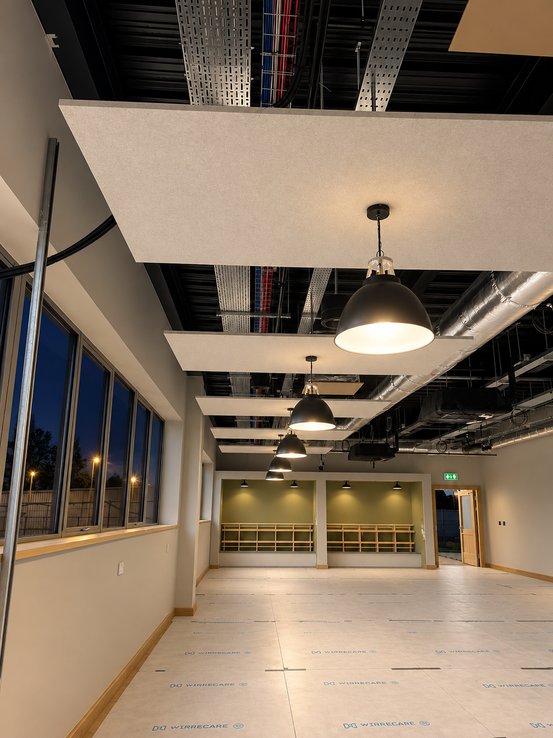 Empty room with large windows, ceiling lights, and unfinished flooring, possibly a dance studio or office space under construction.