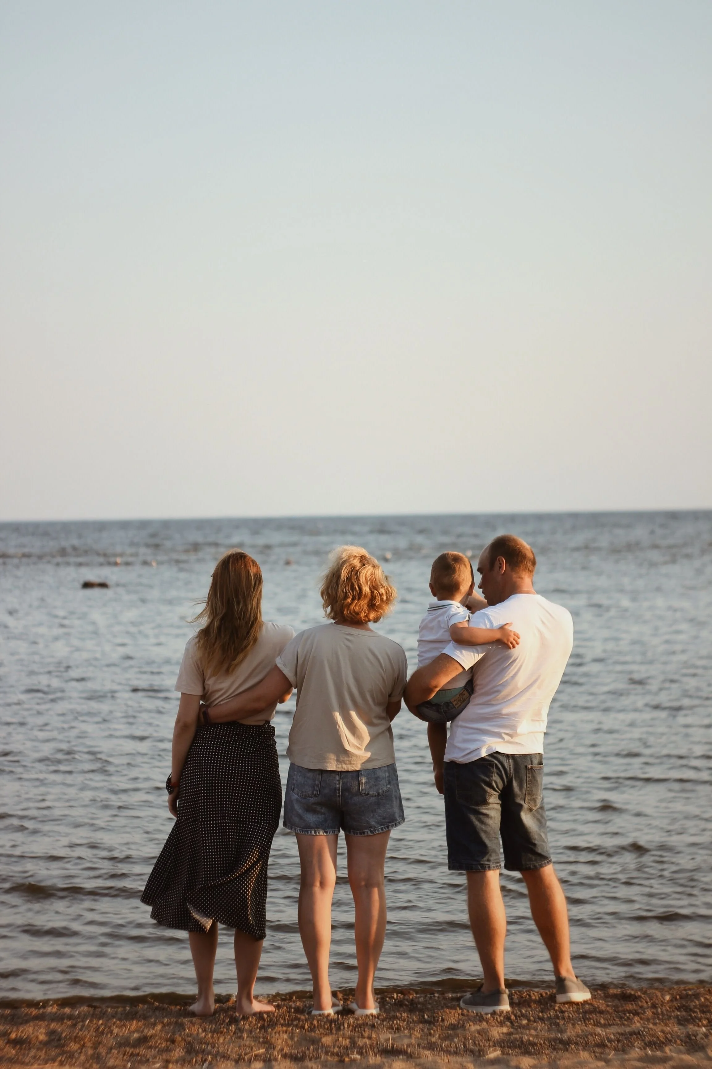 A family of four stands at the water's edge on a beach, looking at the ocean during sunset, while planning for the future
