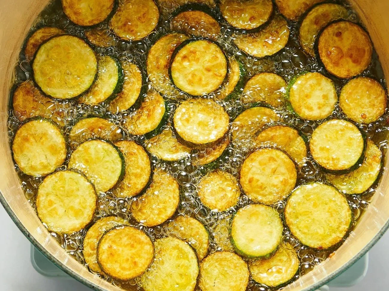 Sliced zucchini rounds frying in hot oil in a pan.