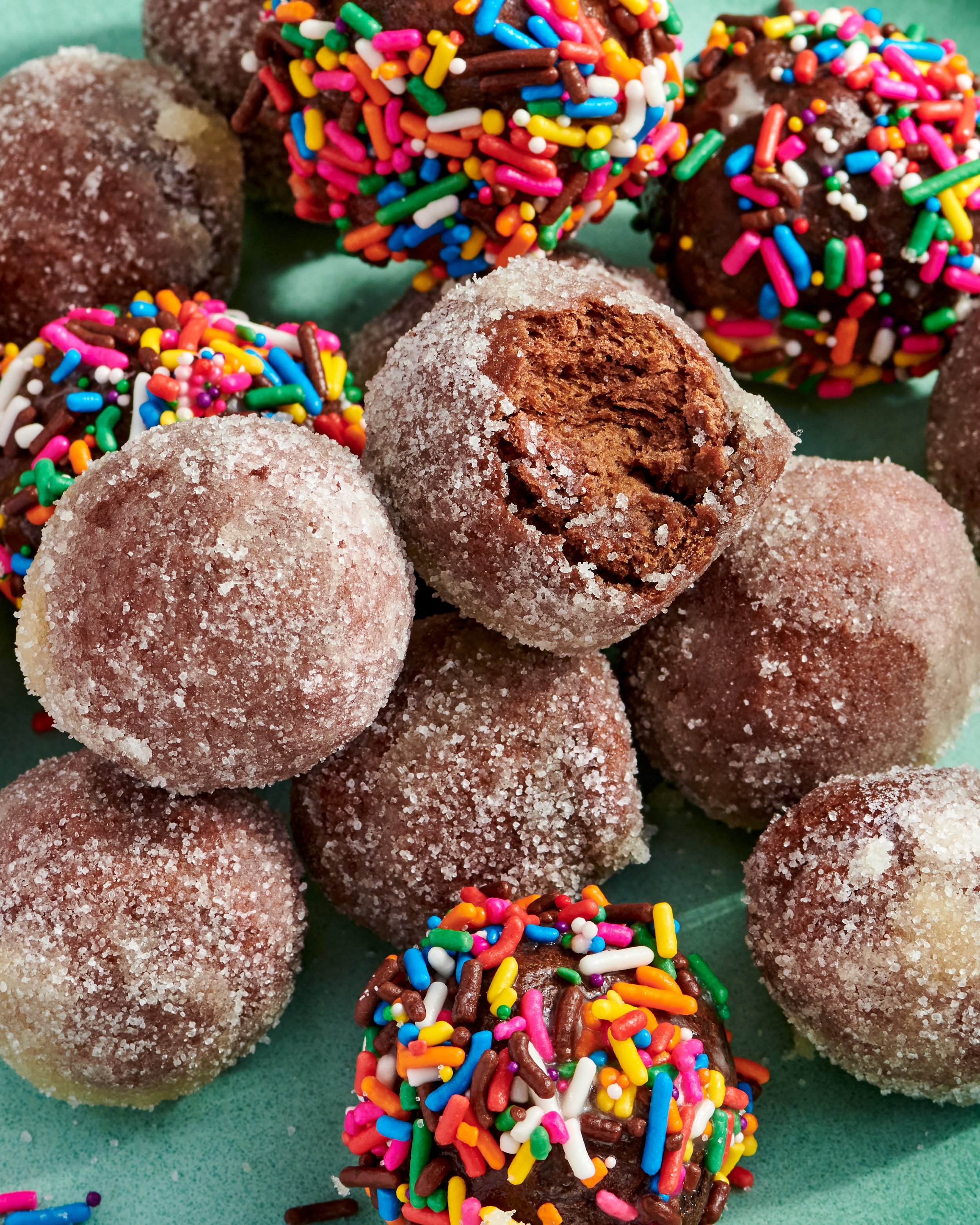 Close-up of chocolate cake balls covered in sugar and colorful sprinkles, on a green surface.