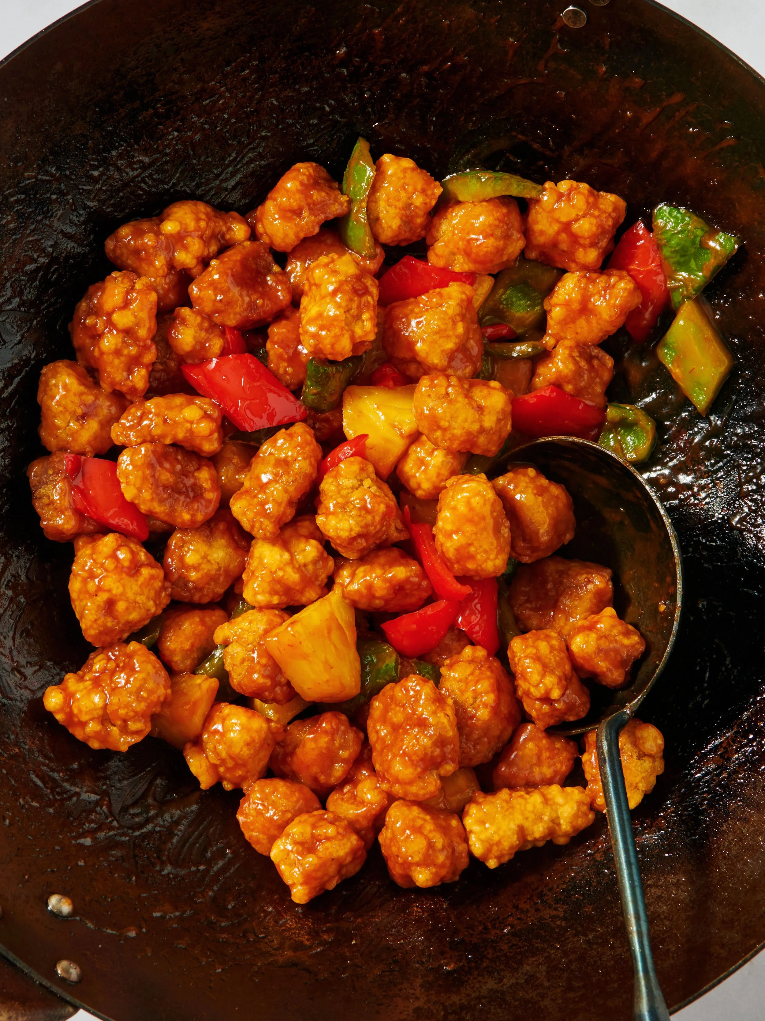 Sweet and sour chicken with pineapple chunks, green and red bell peppers in a wok.