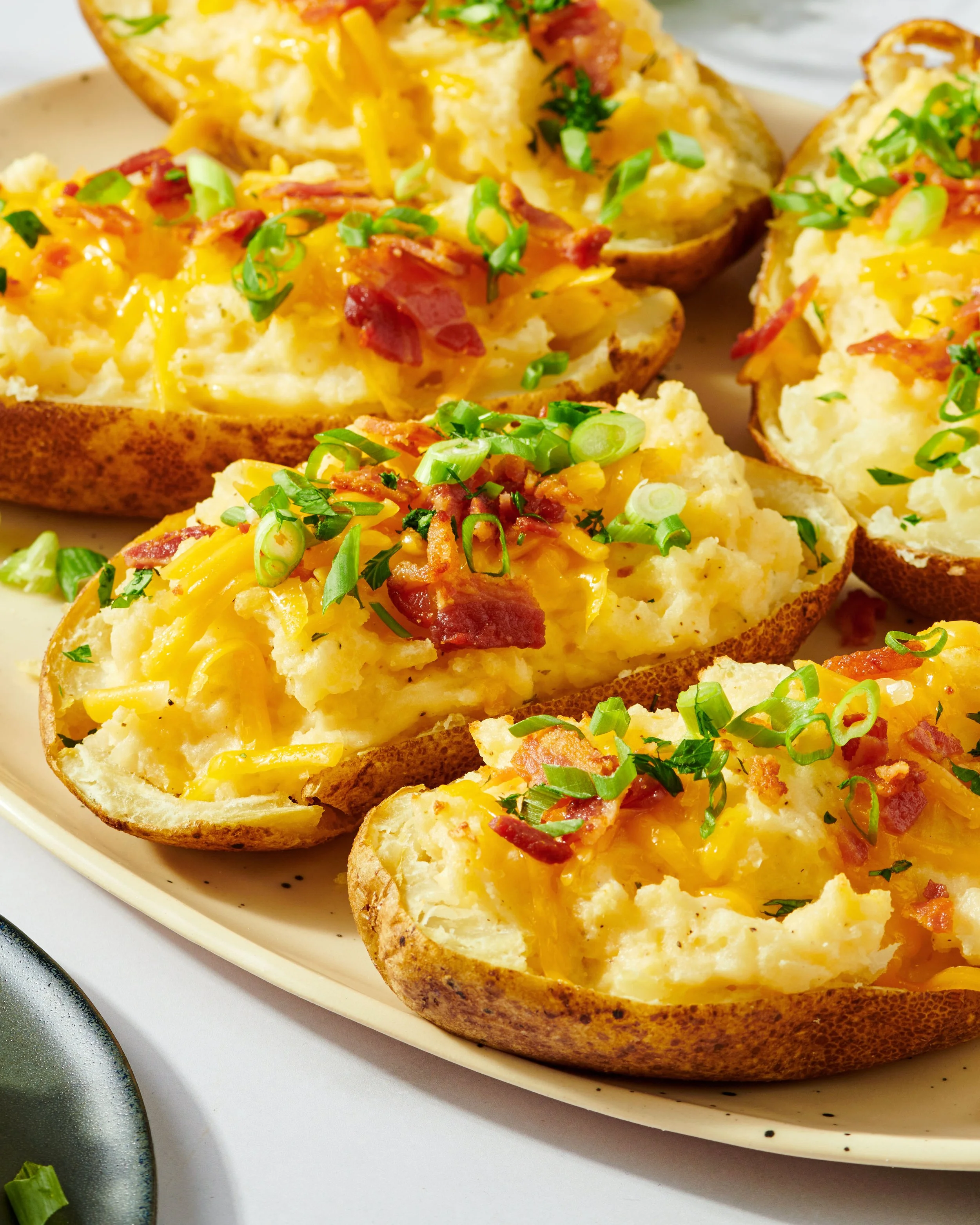 Close-up of loaded baked potato halves topped with shredded cheddar cheese, chopped green onions, bacon bits, and parsley on a white plate.