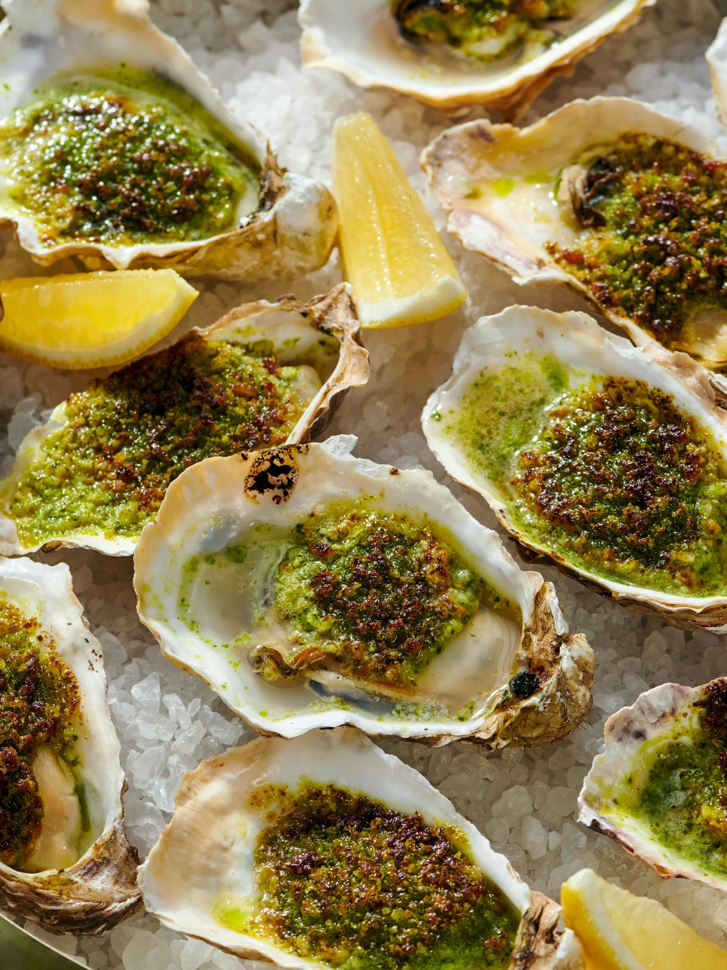 Close-up of oysters on ice with green sauce and lemon wedges.