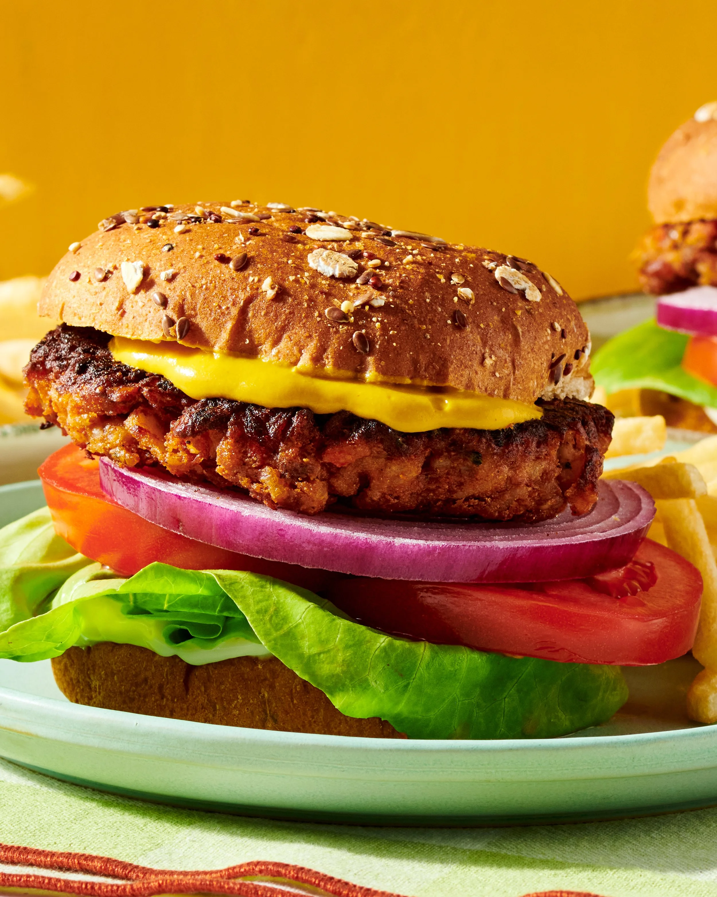 Close-up of a cheeseburger with lettuce, tomato, onion, pickles, and a seeded bun, on a white plate.