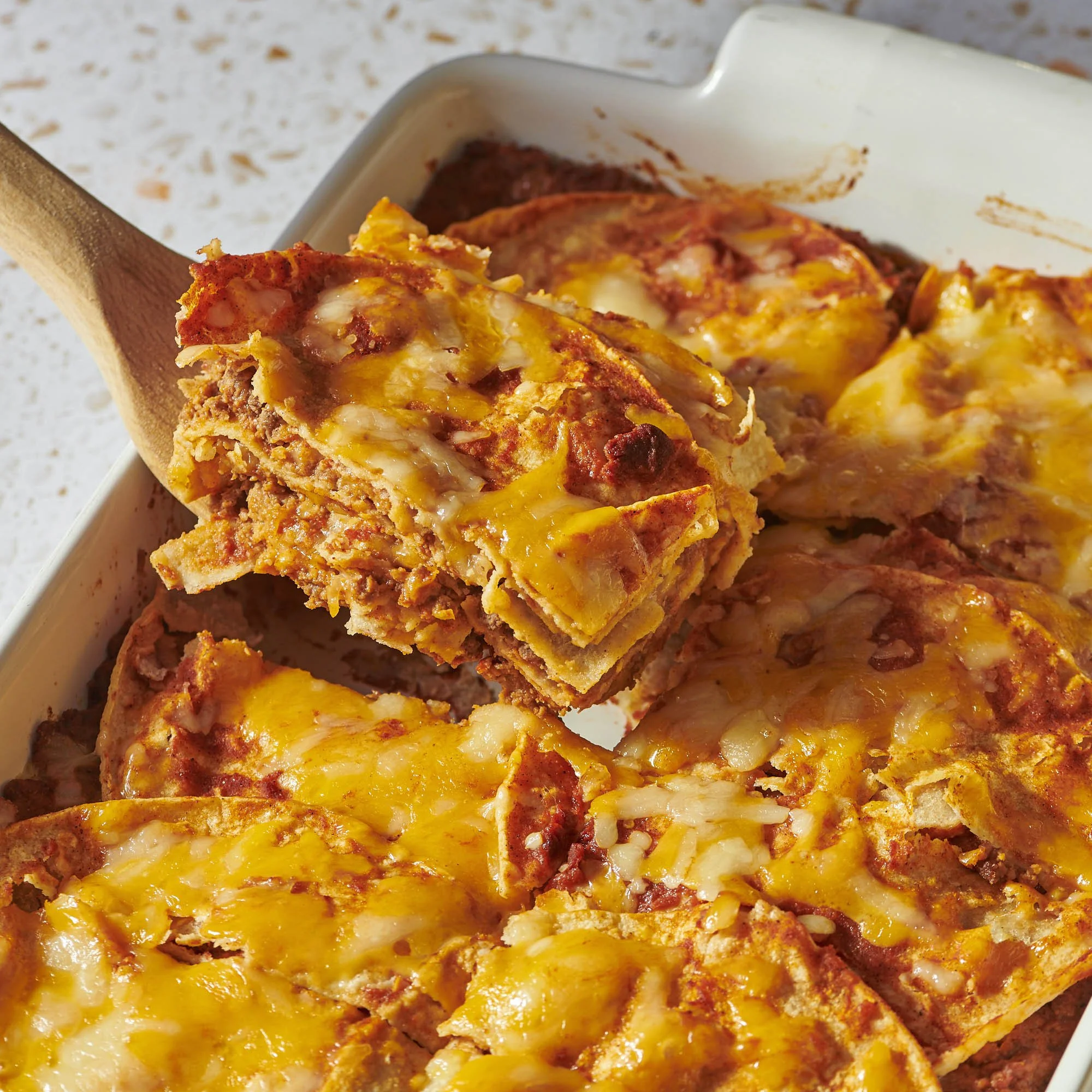 Close-up of a casserole dish filled with layered lasagna, showing melted cheese, tomato sauce, and cooked meat.