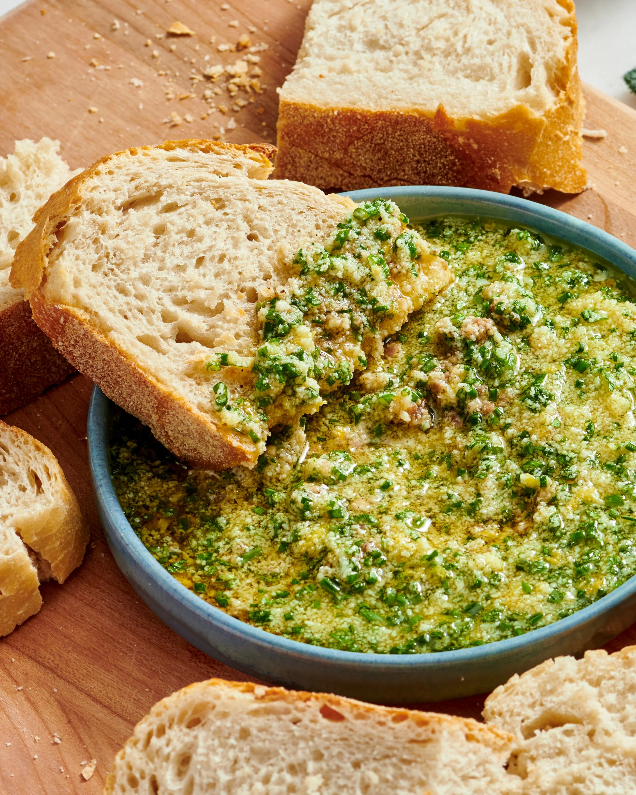 Bread slices and a bowl of herb hummus on a wooden surface.