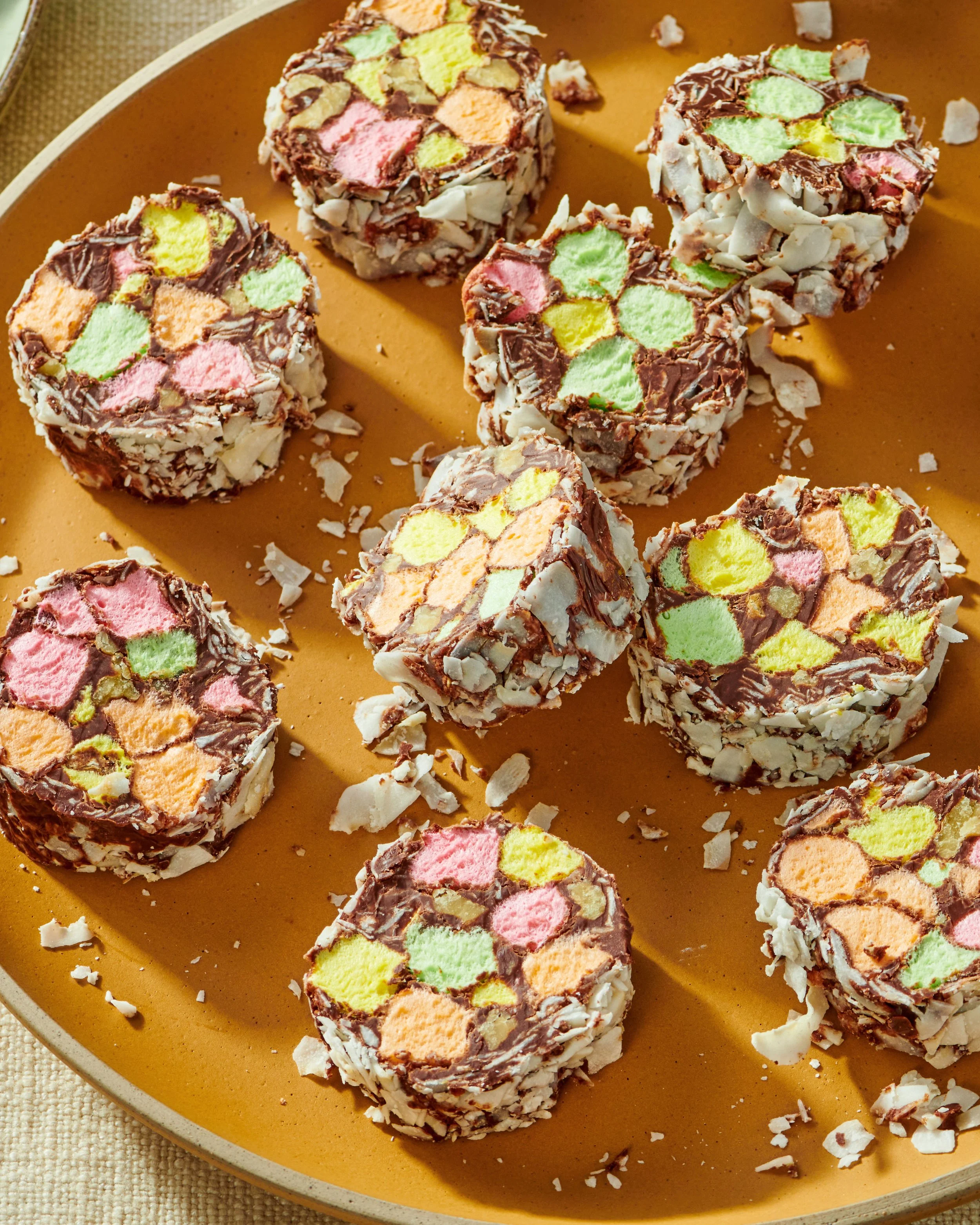 An orange plate with several sliced ice cream cake rolls with colorful ice cream filling and coated with white chocolate and coconut flakes.