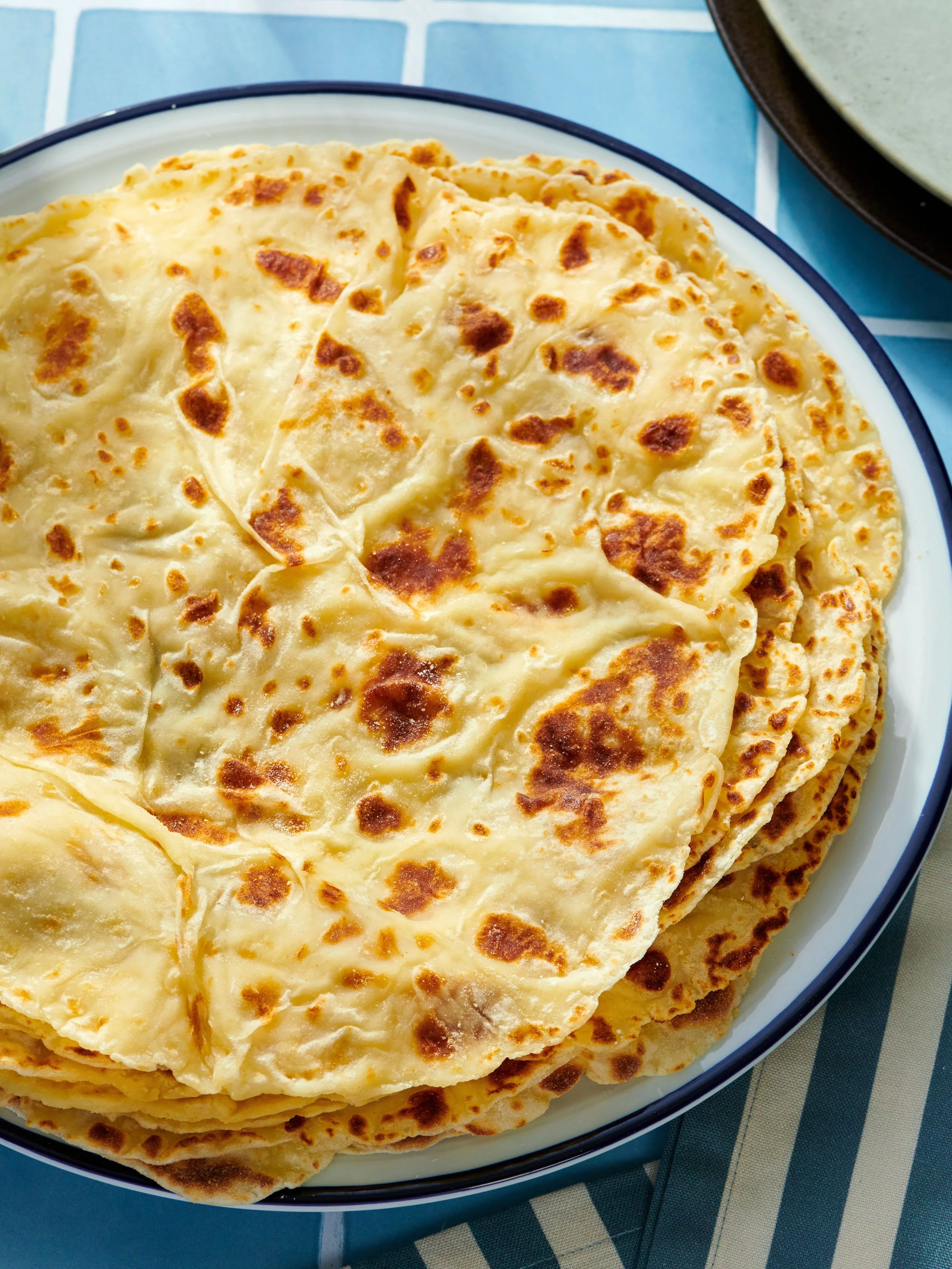 Stack of cooked quesadillas on a white plate with a dark border, placed on a blue and white checkered tablecloth.