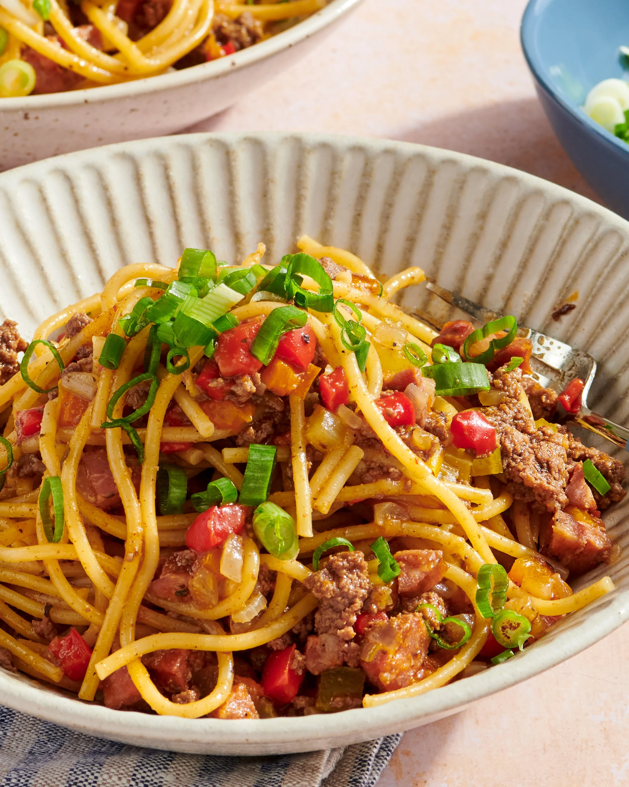 Spaghetti with ground beef, diced tomatoes, and chopped green onions in a white bowl.
