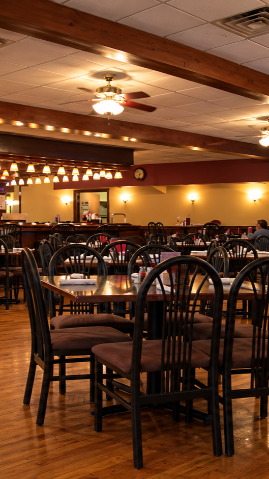 Empty restaurant dining area with wooden tables and chairs, ceiling fans, and warm lighting.