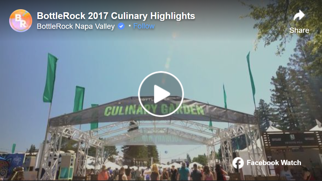 An outdoor event at BottleRock Napa Valley with a large white tent labeled "Culinary Garden" and several green flags, crowd of people walking underneath, blue sky and trees in the background.