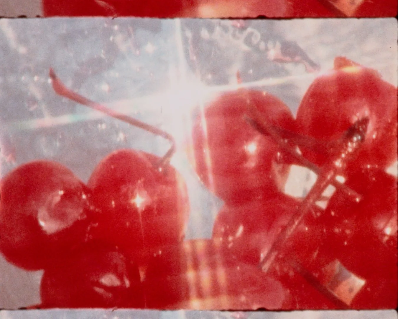 A close-up of a few red cherries, with a bright light shining behind them, creating a starburst effect.