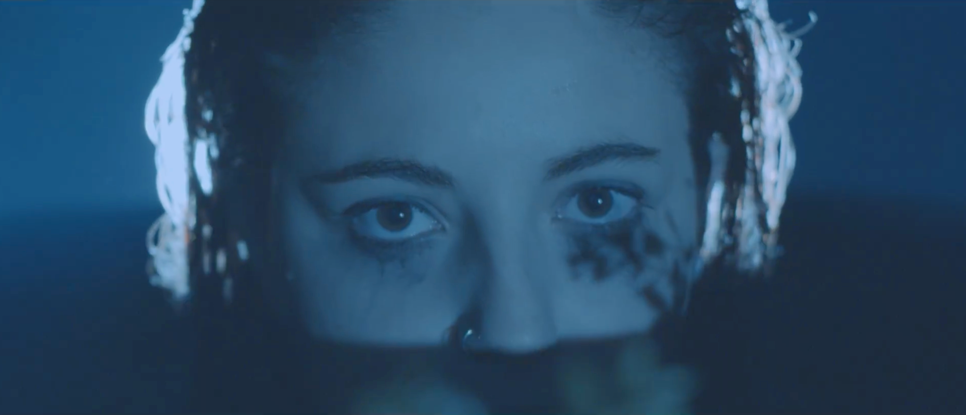 Close-up of a person's face emerging from water with intense eyes, predominantly blue tones.