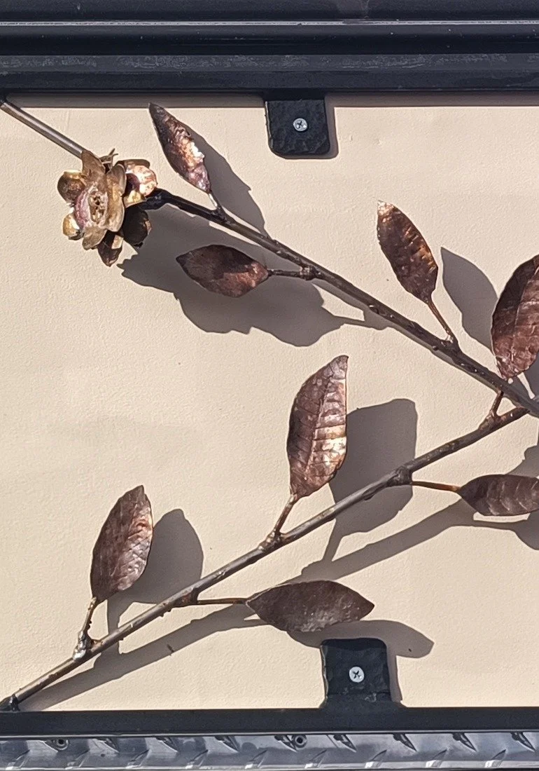 Decorative metal vine with hand-formed leaves and a rose, mounted on a truck canopy panel
