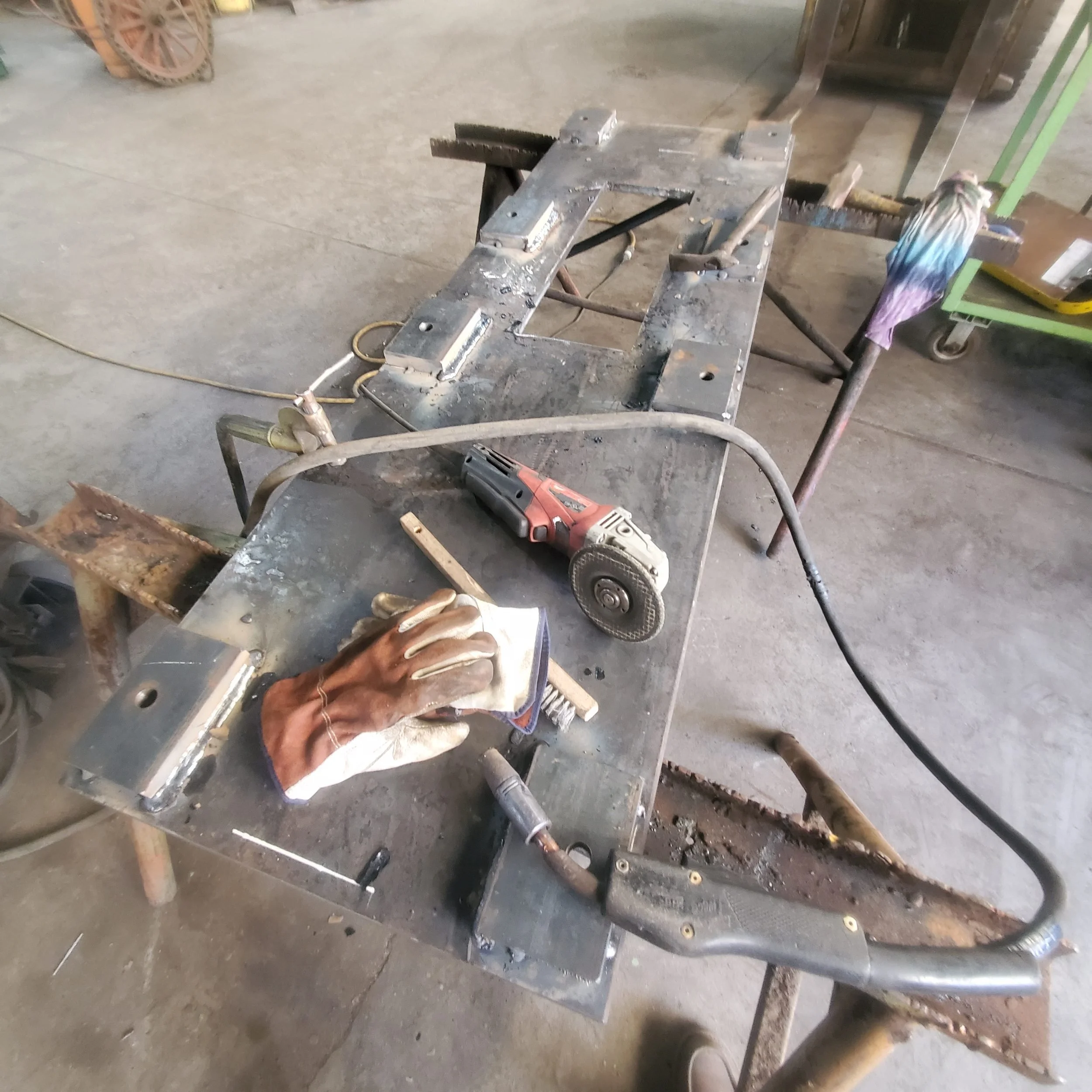 Industrial winch support base being fabricated from one-inch steel plate, with an angle grinder and welding gloves