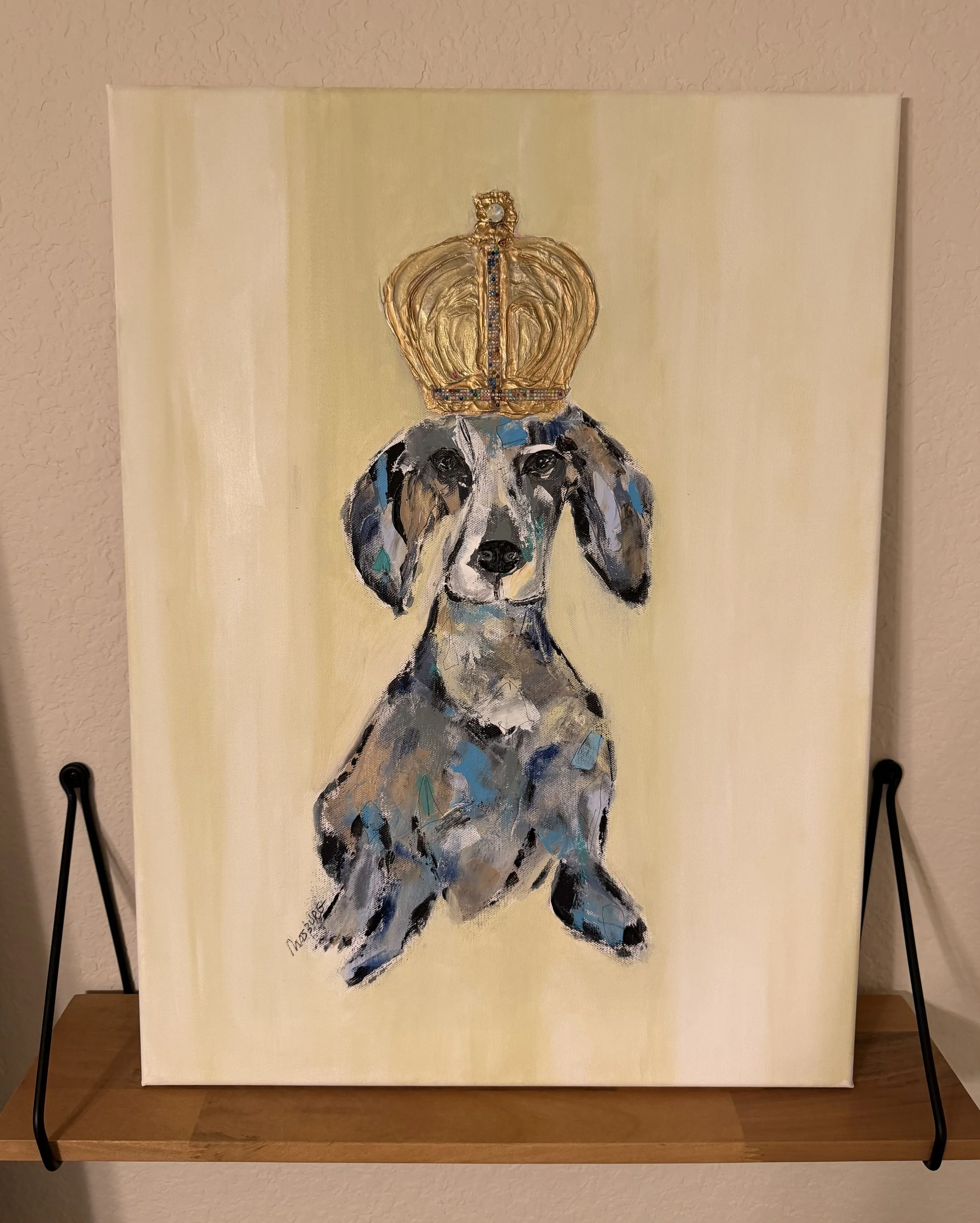 Painting of a dog with a crown on its head, created in an abstract, colorful style, displayed on a stand.
