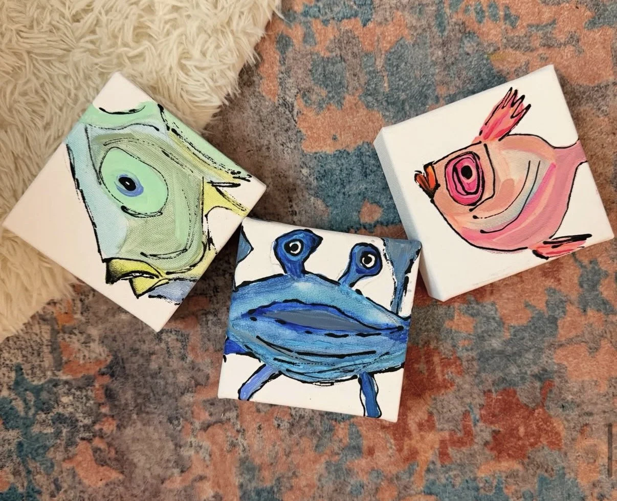 Three small canvas paintings of animals - a frog, a crab, and a bird, placed on a colorful textured rug near a fluffy beige rug.