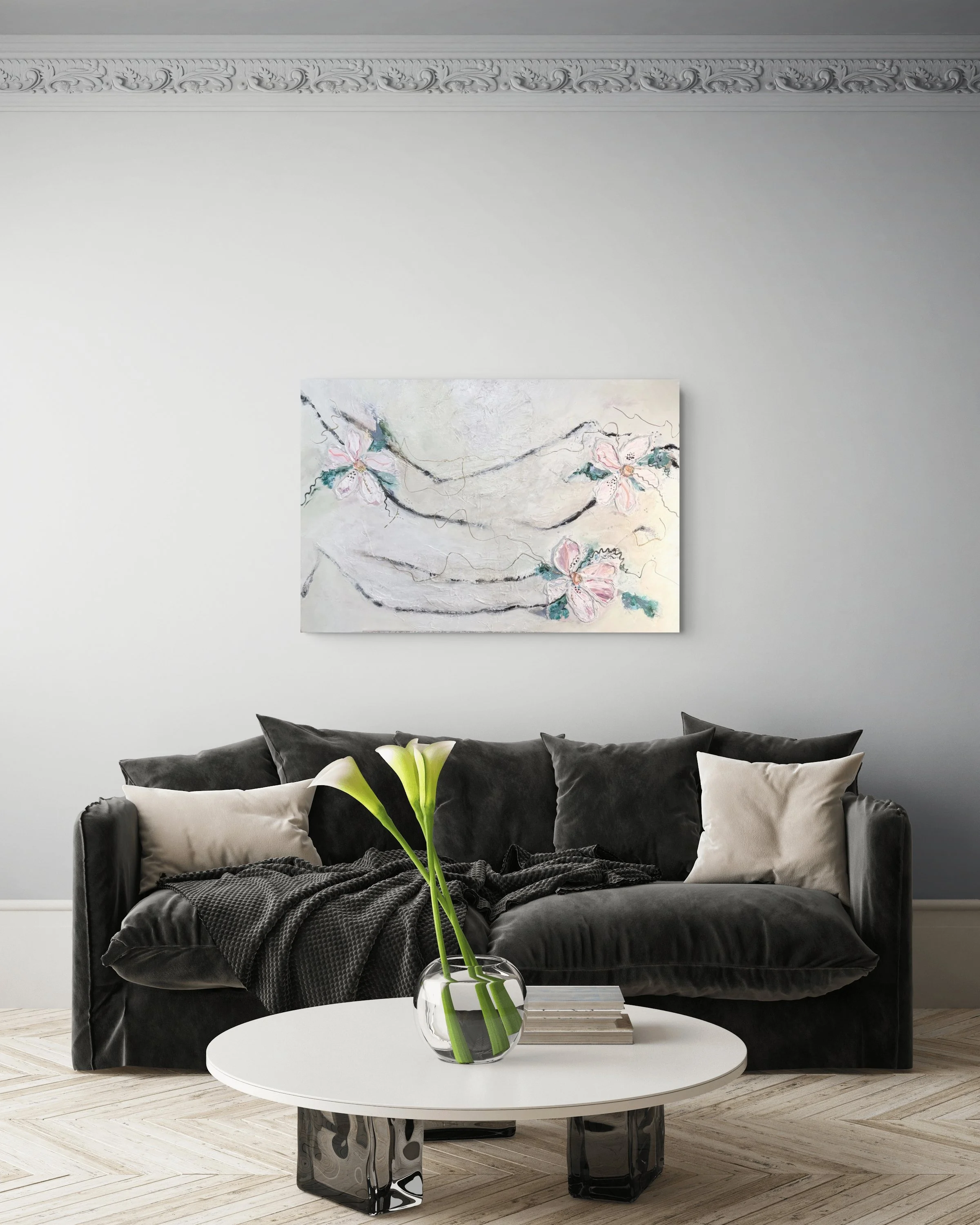 Modern living room with black velvet sofa, beige and black pillows, a white round coffee table with a glass vase containing white lilies, a black decorative object, a colorful abstract painting of flowers on the white wall, and a light wood patterned floor.