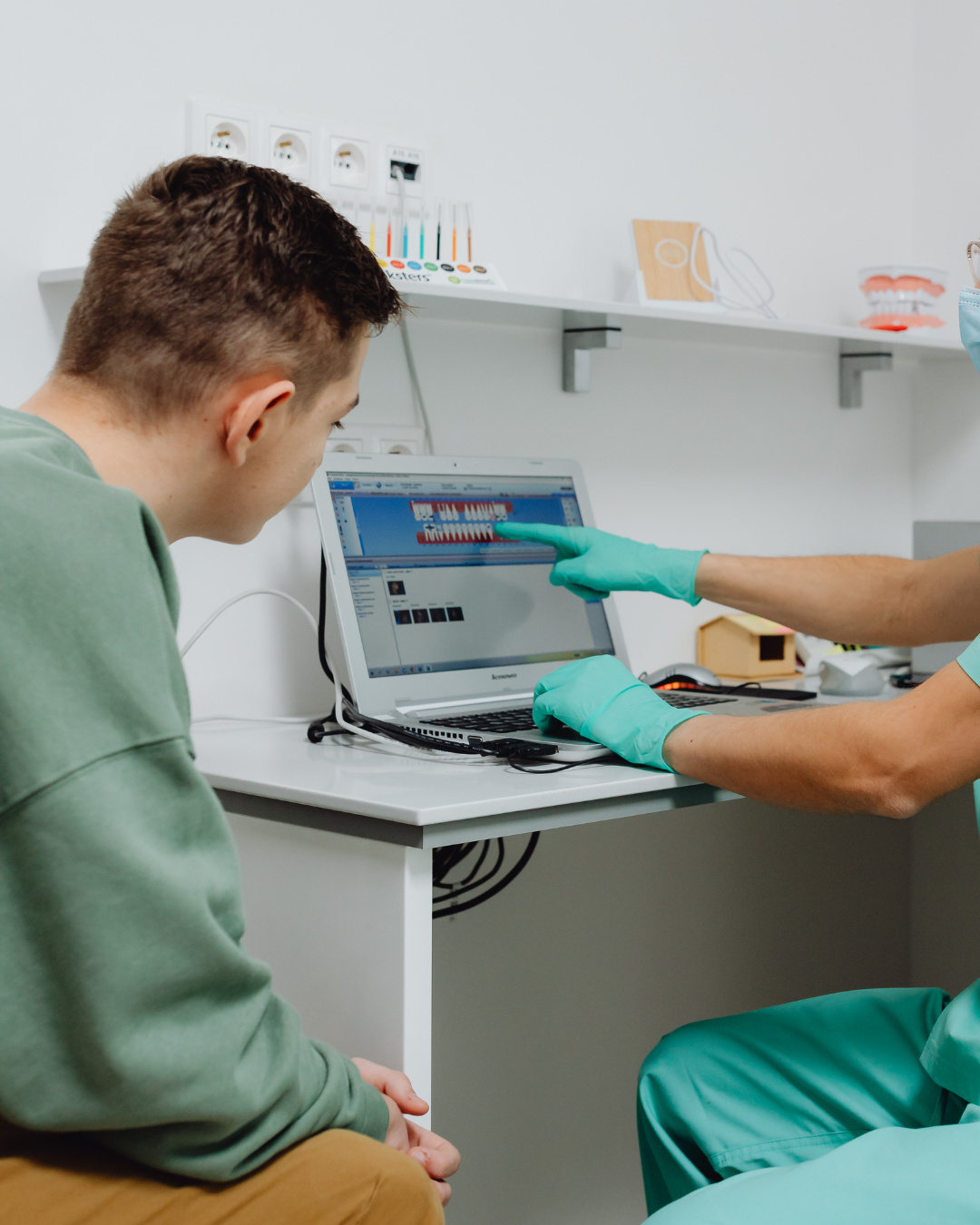 Paciente observando uma tela de computador com imagens de dente, enquanto profissional de odontologia aponta para ela.