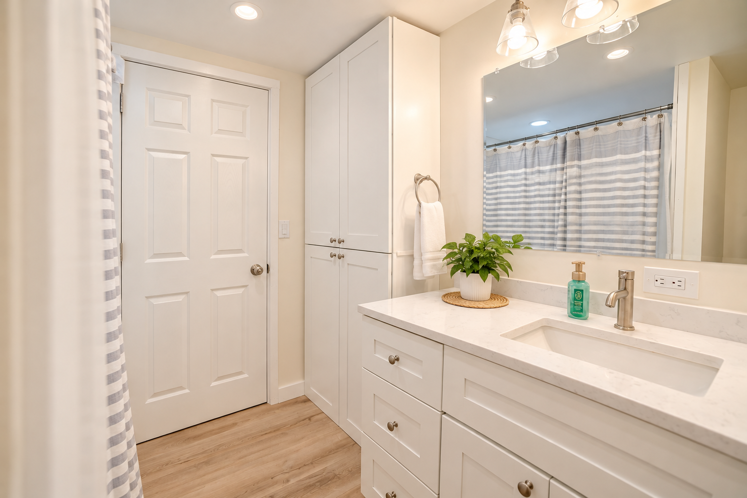 Bright white bathroom with double vanity, marble countertop, large mirror, striped shower curtain, linen storage cabinet, and potted plant.