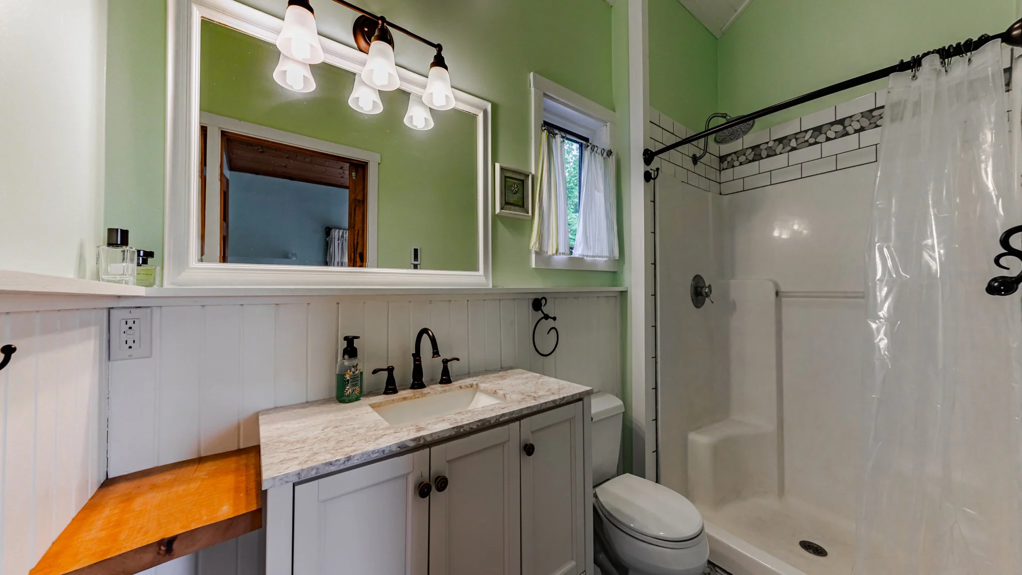 Bright green and white bathroom with vanity, framed mirror, black fixtures, toilet, and tiled shower with glass doors