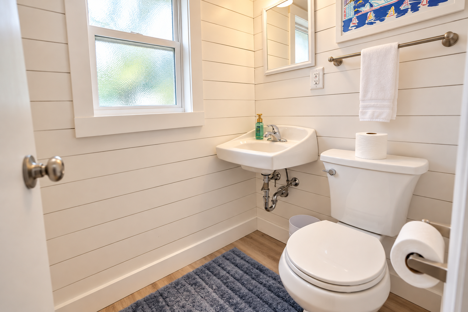 Clean compact bathroom with a pedestal sink, toilet, frosted window, white towel, and blue bath mat