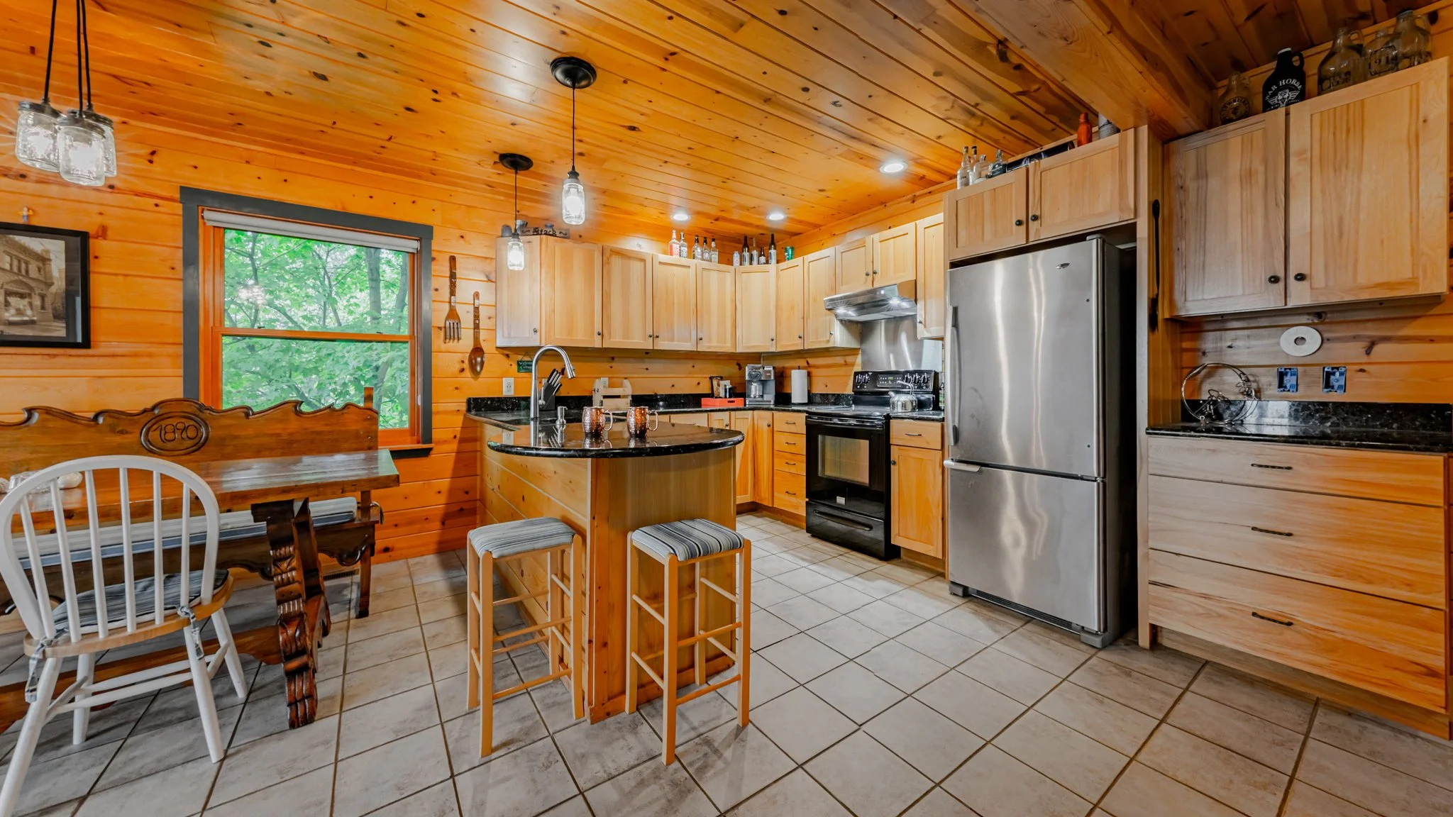 Rustic wood-paneled kitchen with an island, bar stools, stainless steel appliances, wooden cabinets, and dining table