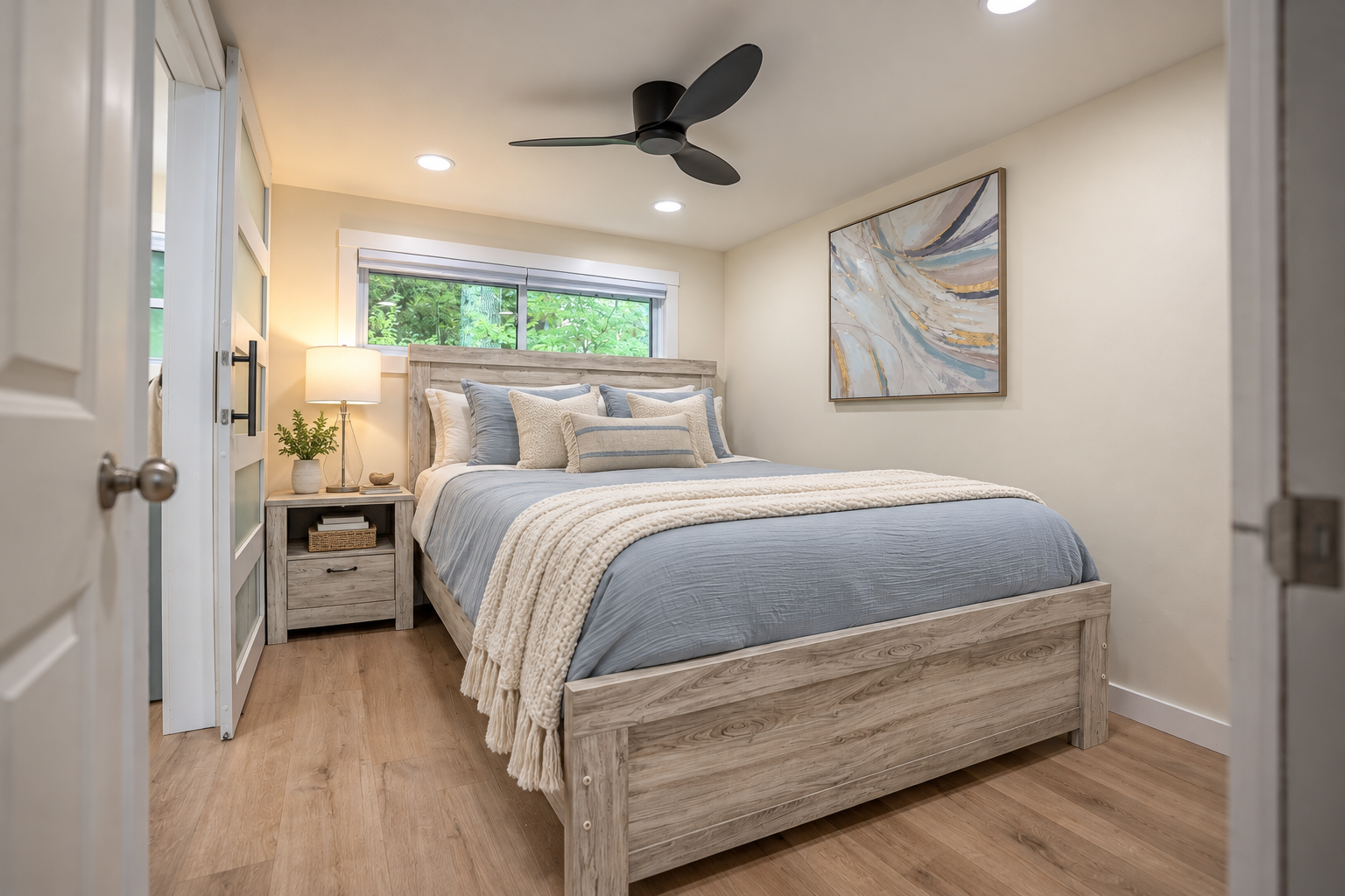 Cozy bedroom with a wood bed, blue bedding, cream throw blanket, ceiling fan, nightstand, and abstract wall art.