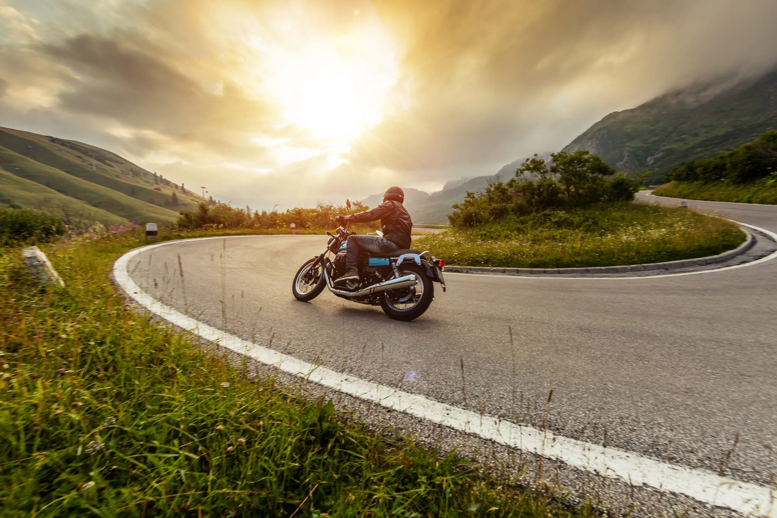 Motorcycle leaning into a curve on a road at sunset.