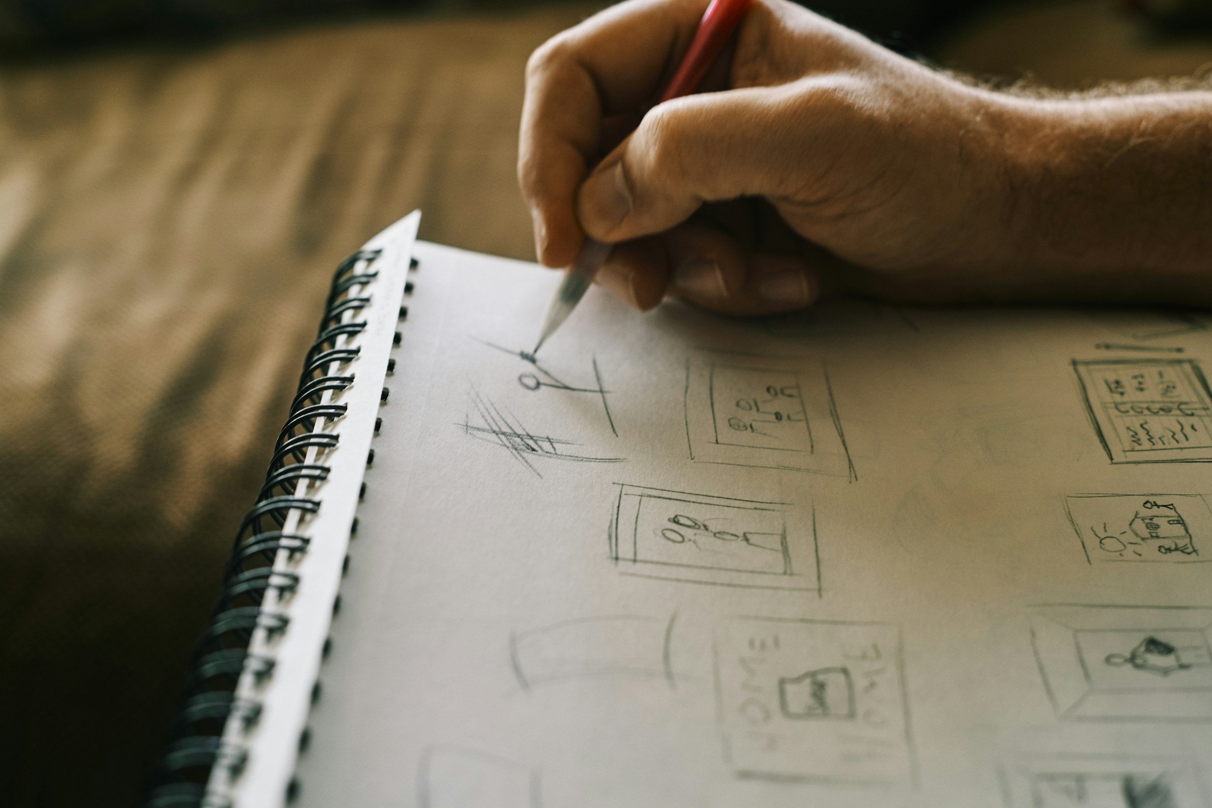 Hand holding a pencil, sketching small illustrations on a sketch pad.
