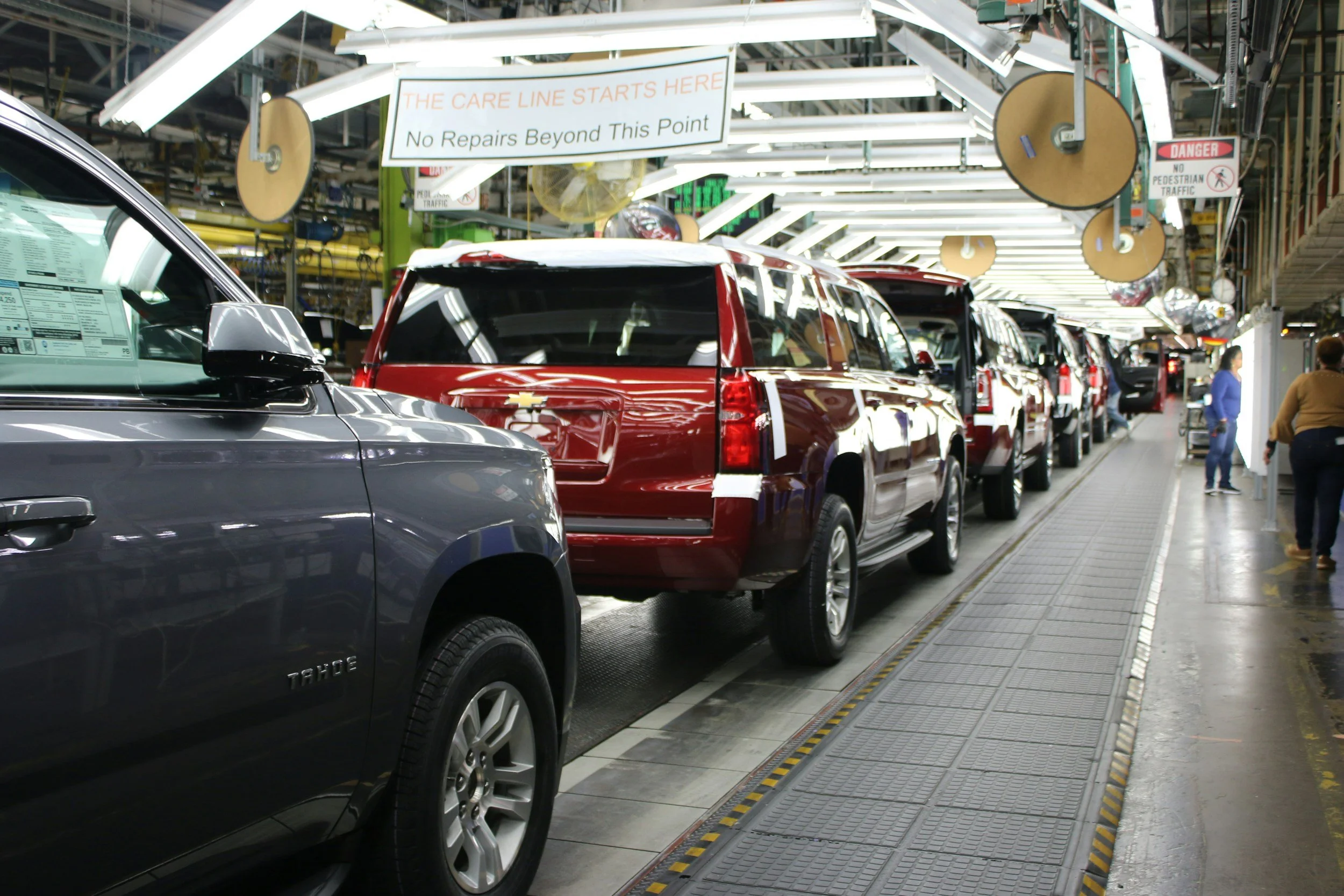 Inside an automotive service center with several parked cars and overhead signs, including one that reads 'The Care Line Starts Here No Repairs Beyond This Point' and another 'Danger No Pedestrian Traffic'.