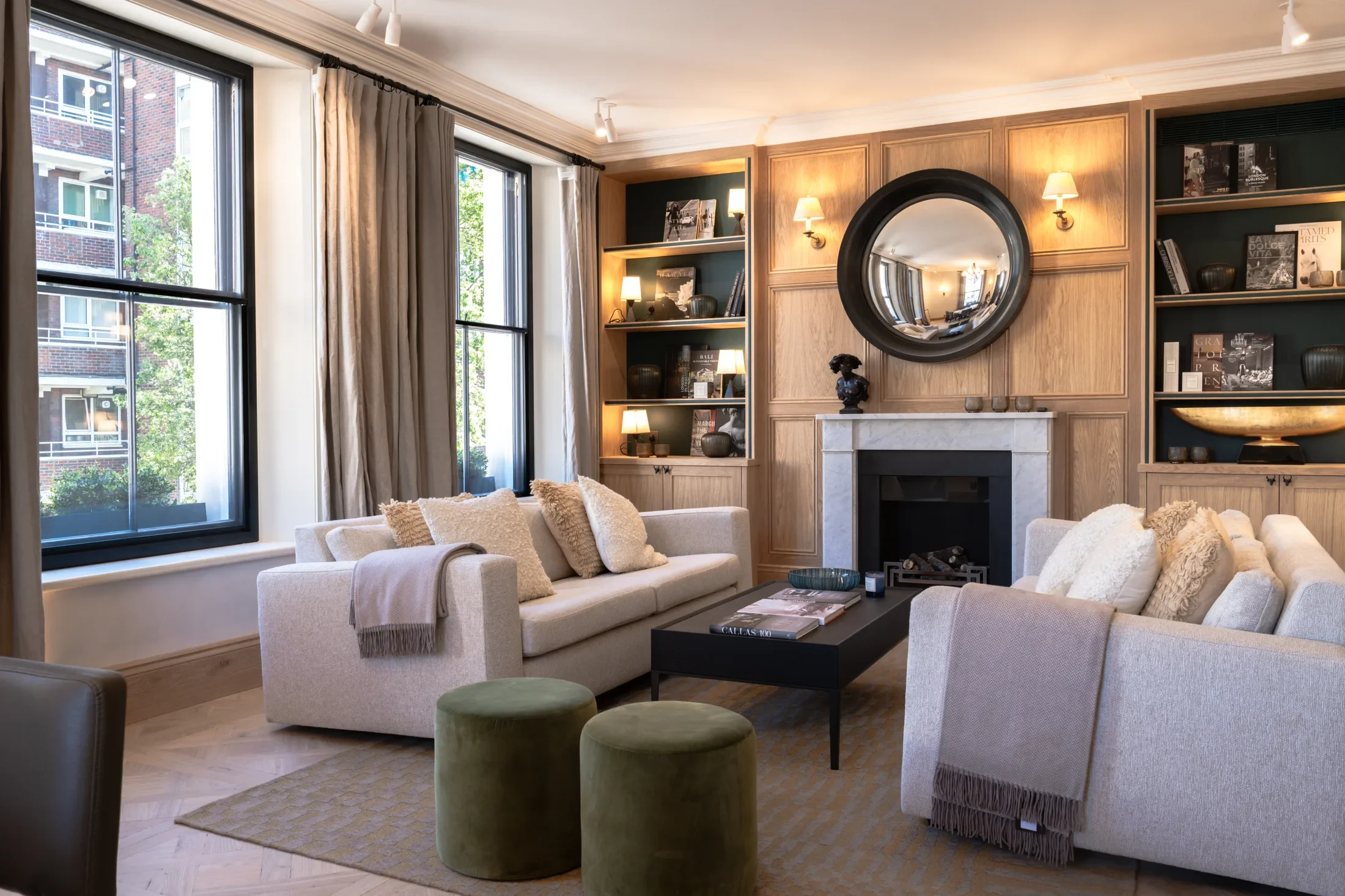 Sitting room with a fireplace, round mirror and garden-facing windows — AKC Asset Management real estate, part of AKC Group.